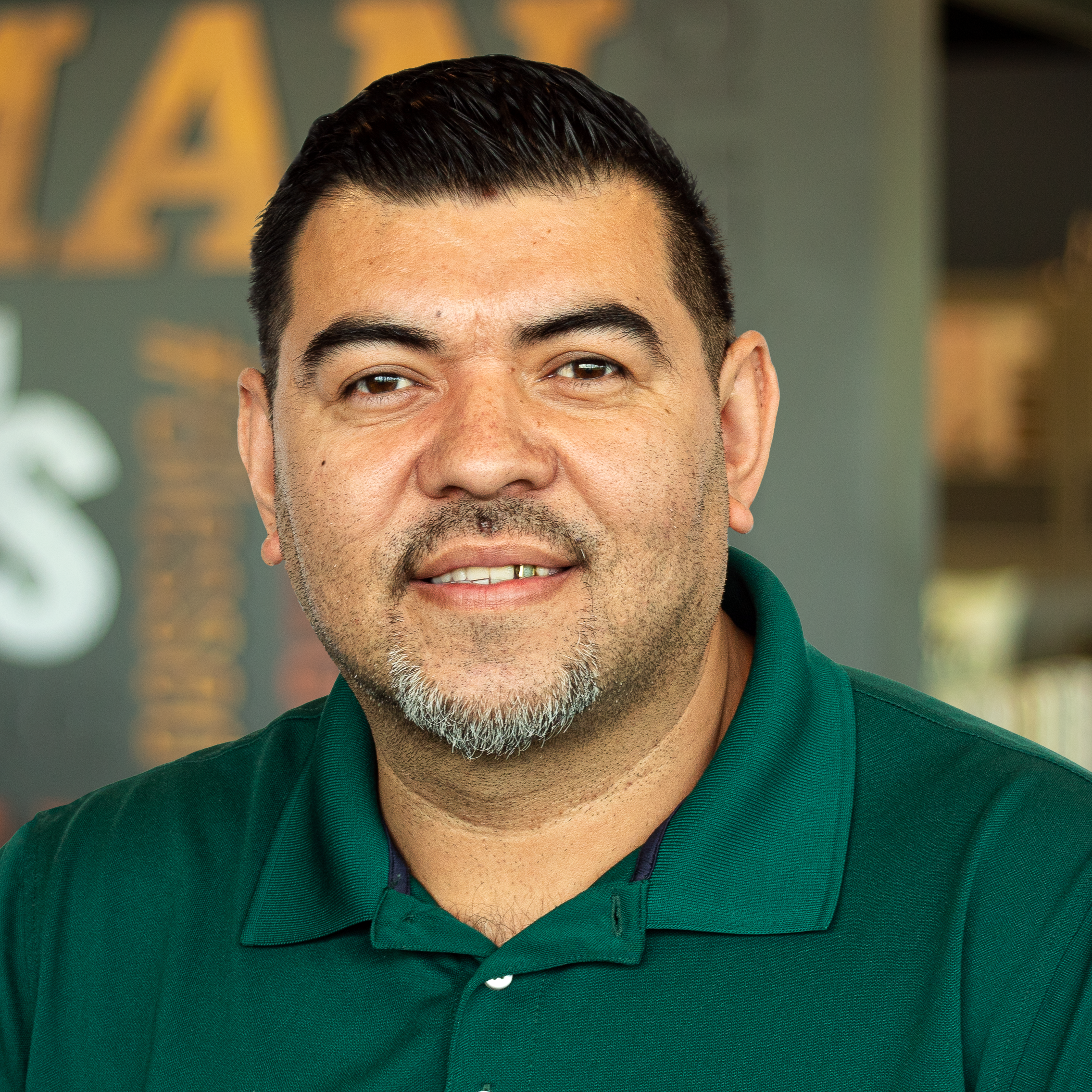 Santos Reyes wearing a green polo and standing in front of a company-branded wall.