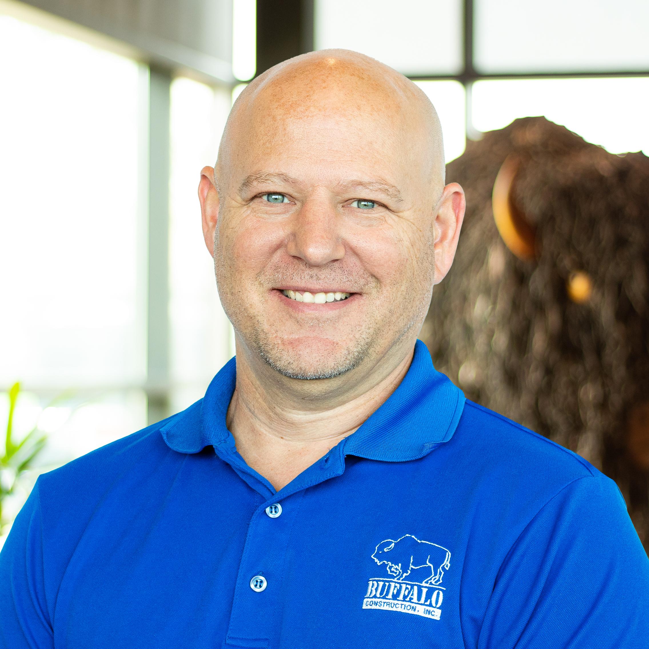 Tony Dulceak wearing a bright blue buffalo branded polo and smiling as they stand in front of a statue of a buffalo.