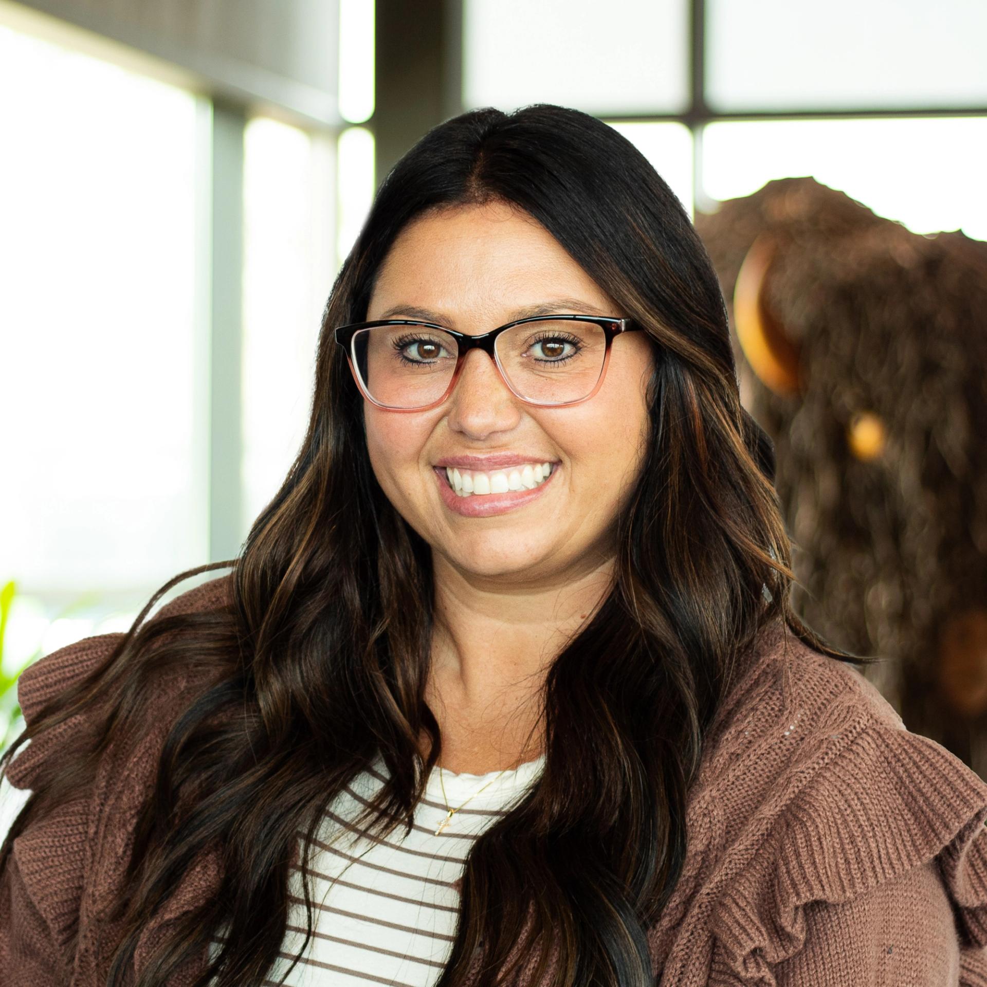 Bri Pfeiffer wearing a taupe blazer, smiling for the camera in a bright, modern office.