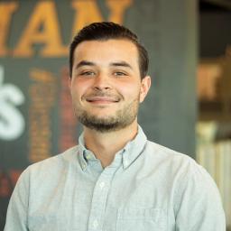 Preston Pearl, wearing a button up shirt and standing in front of a company-branded wall.