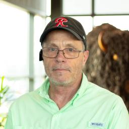 Michael McClarty smiling, wearing a light green button-down shirt and black cap, standing in Buffalo Construction's office space.