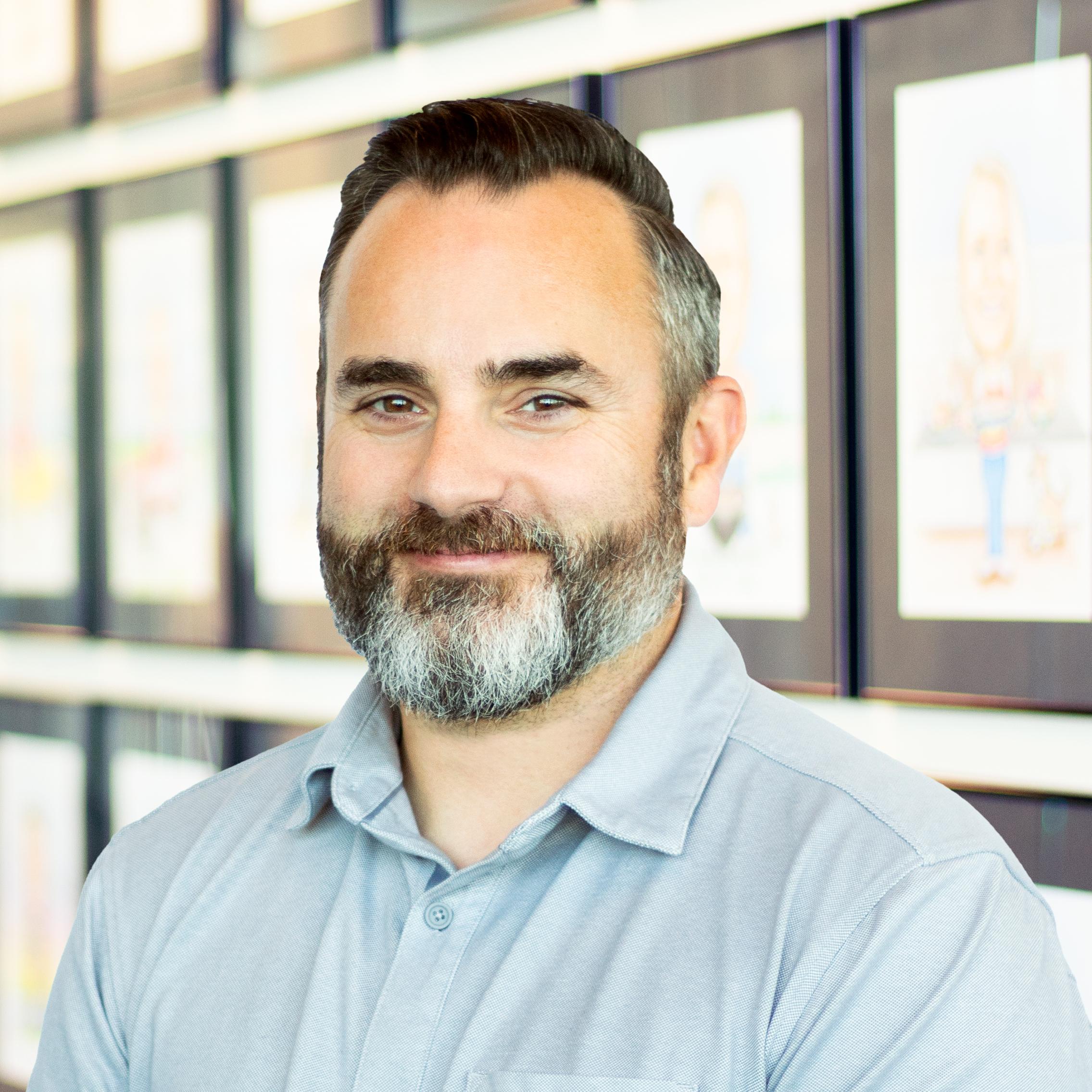 Kristopher Gorter wearing a smile in front of a wall displaying framed caricatures