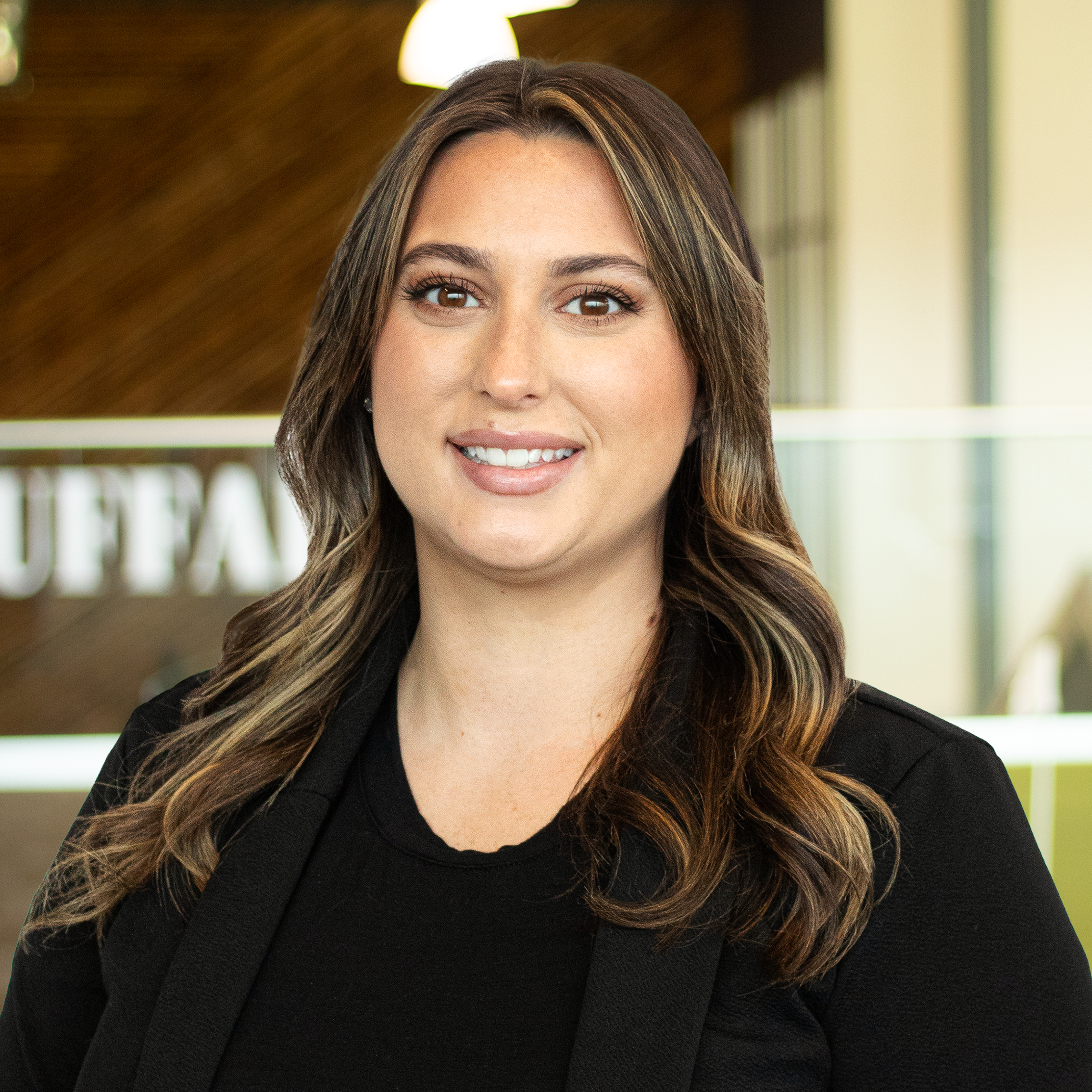 Taryn Day smiling, wearing a black top and black jacket, standing in buffalo's office space.