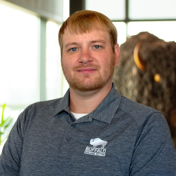 Andrew Szerletich lightly smiling in front of a statue of a buffalo.