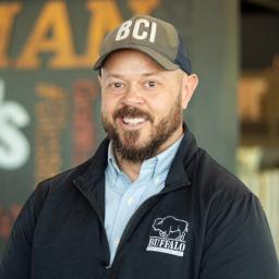 Michael Davis wearing a buffalo branded sweater and standing in front of a company-branded wall.