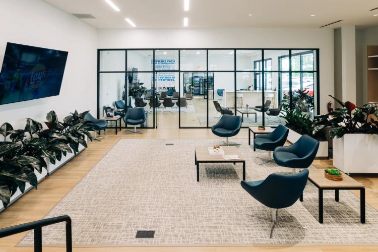Completed customer waiting lounge with blue seating, indoor planters, light wood flooring and glass walls separating adjacent spaces.