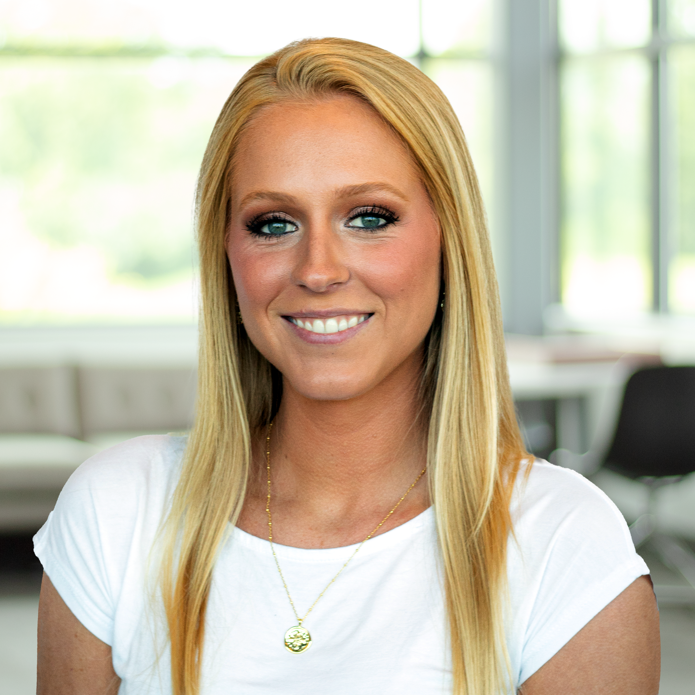 Hailey Baumann wearing a white shirt and a nice smile in a bright, modern office.