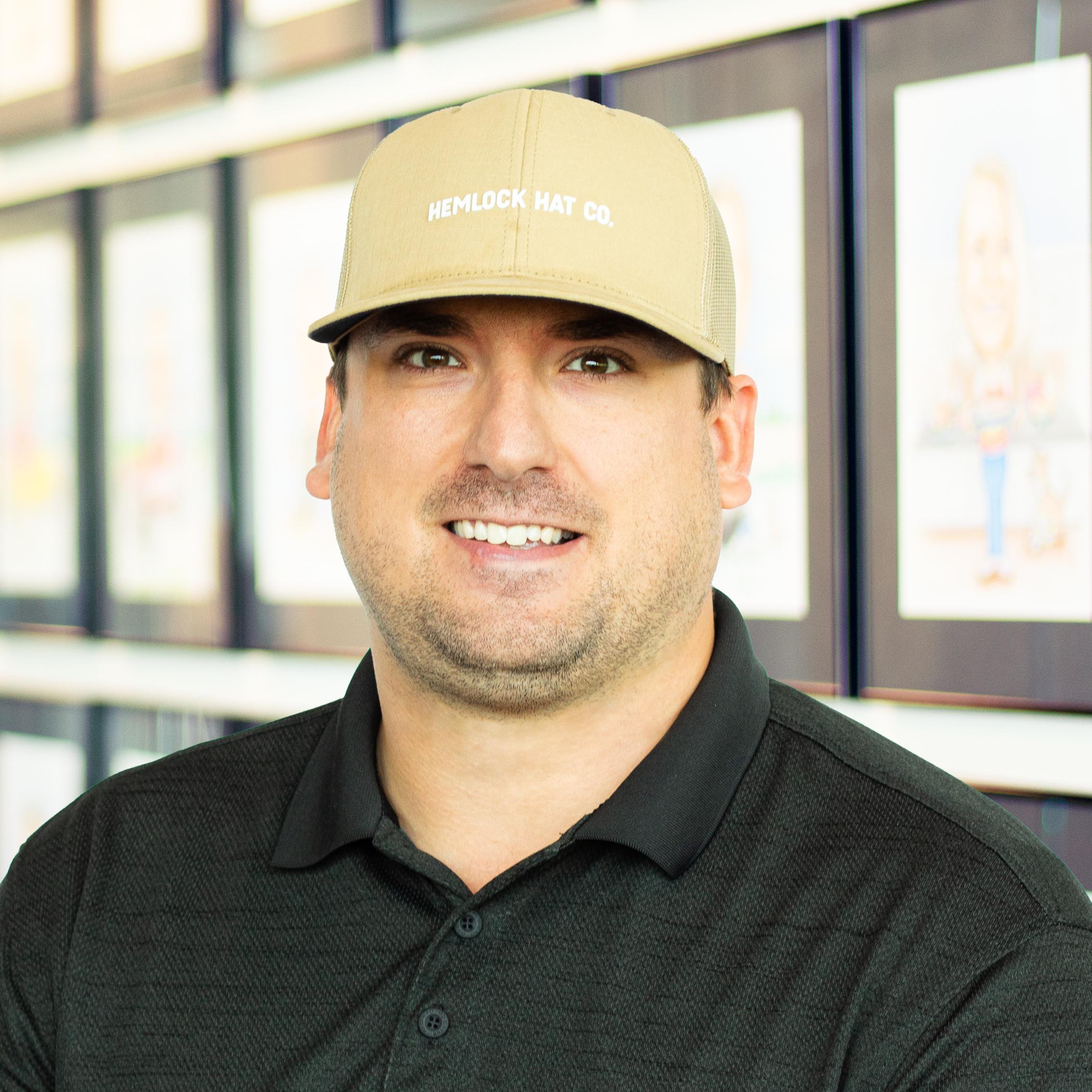 Collin Spink wearing a smile and standing in front of a wall displaying framed caricatures.