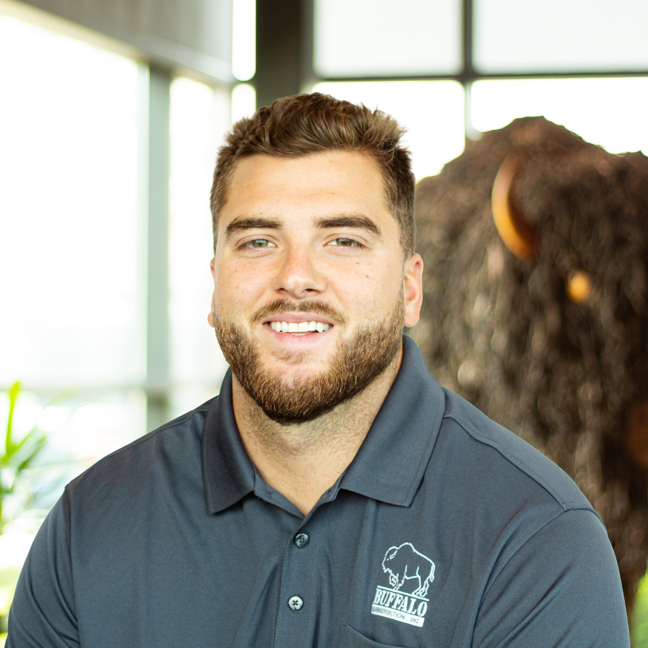 Austin Mock smiling as he stands in front of a statue of a buffalo.