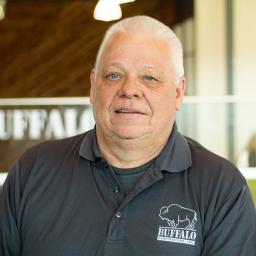 Larry Glidewell with a faint smile, wearing a buffalo construction branded polo and standing in buffalo's office space.