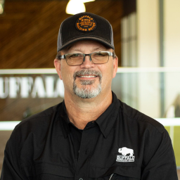 Eric Fleming wearing a black buffalo branded polo and hat, standing in buffalo's office space.