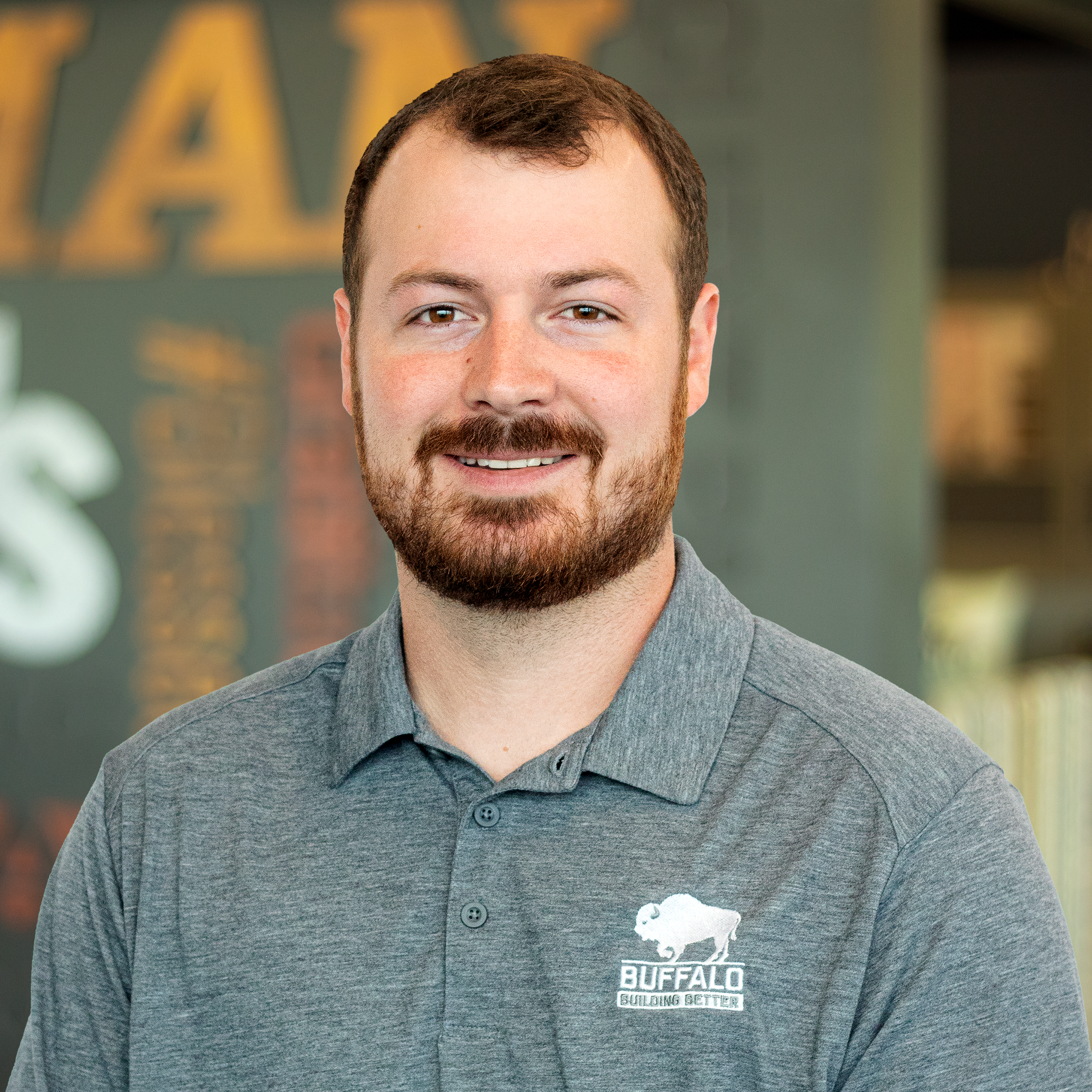 John Brewer smiling, wearing a buffalo branded polo and standing in front of a company-branded wall.
