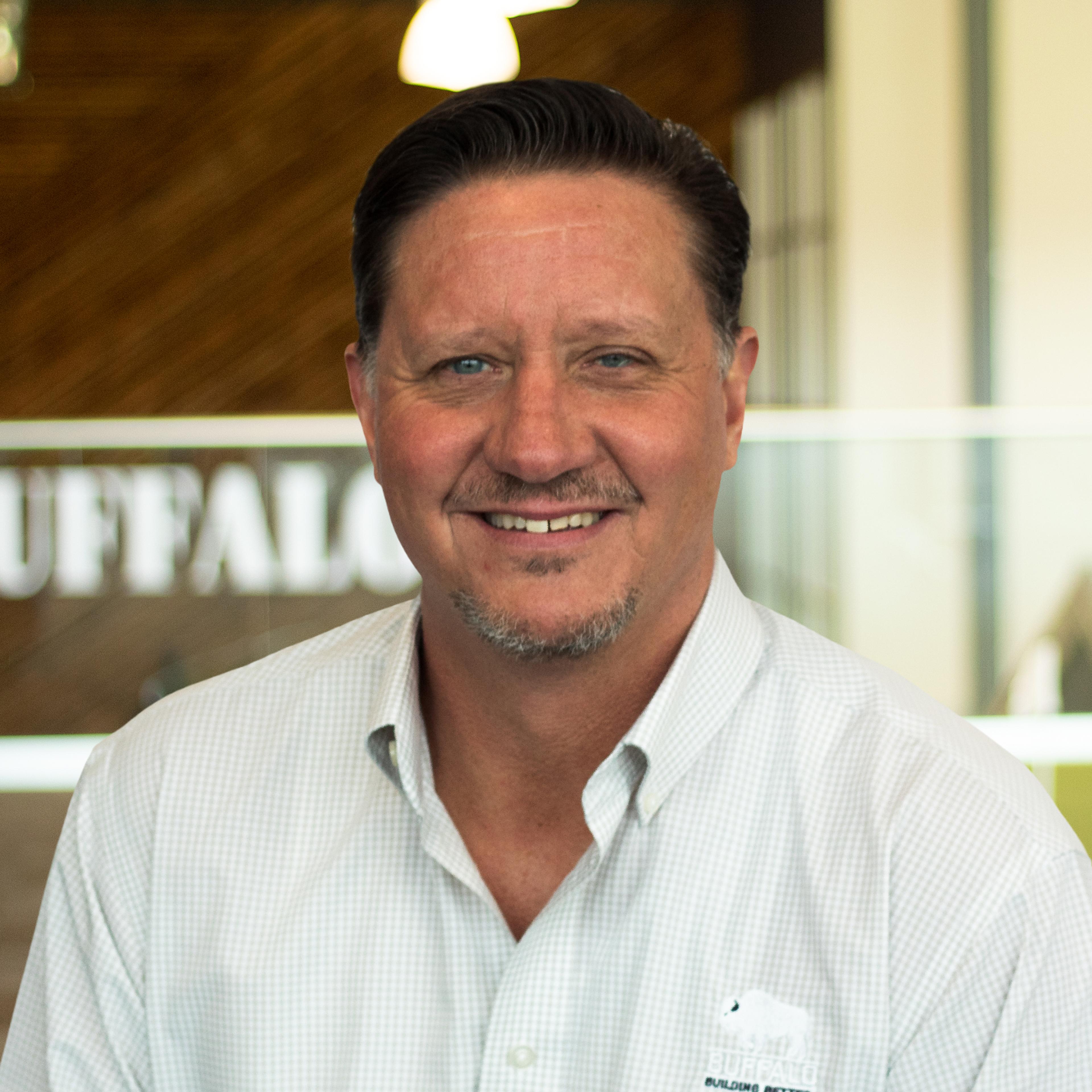 Robert Burns wearing a light button-down shirt and standing in front of a company-branded wall.