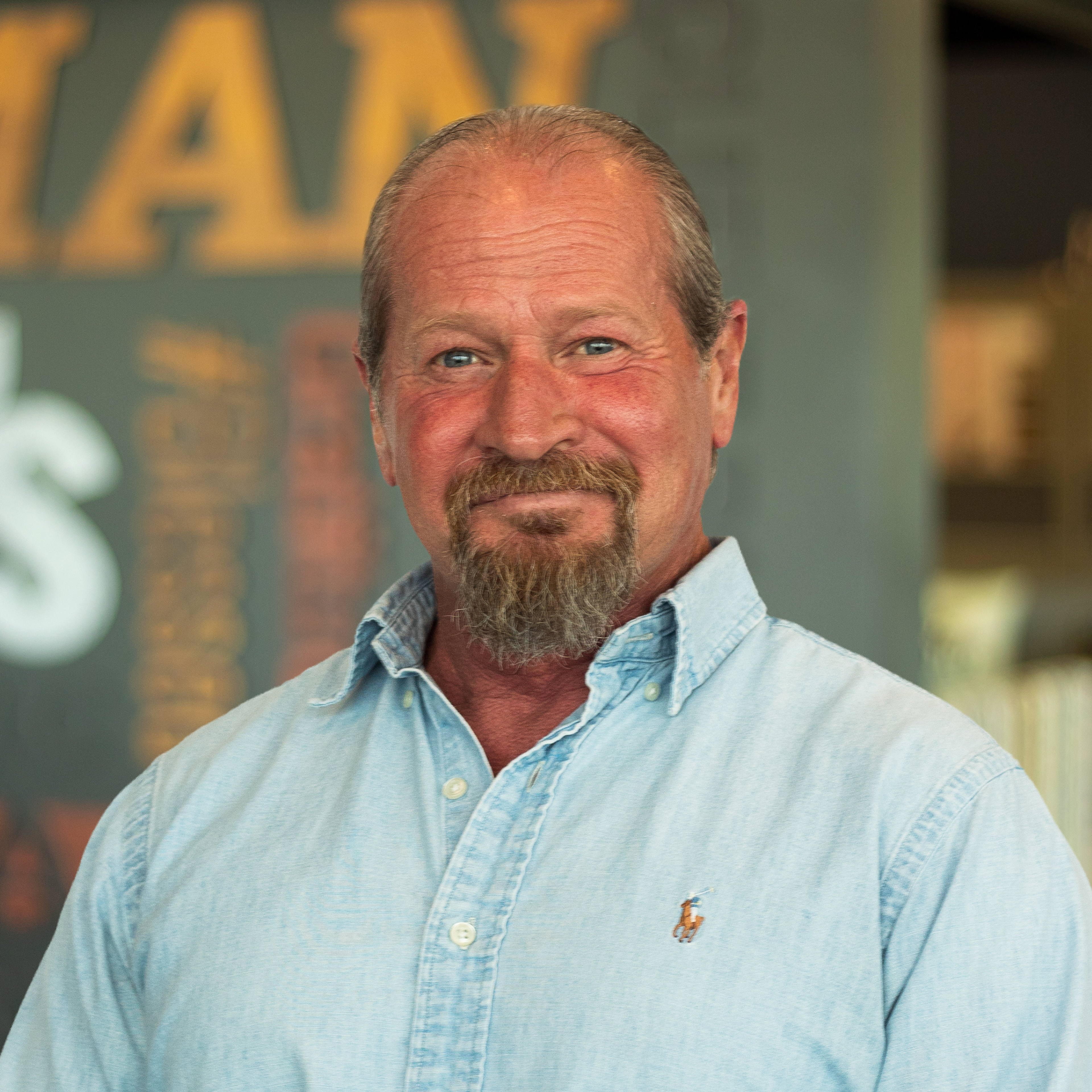David Hobbs wearing a light blue button-down shirt and standing in front of a company-branded wall.