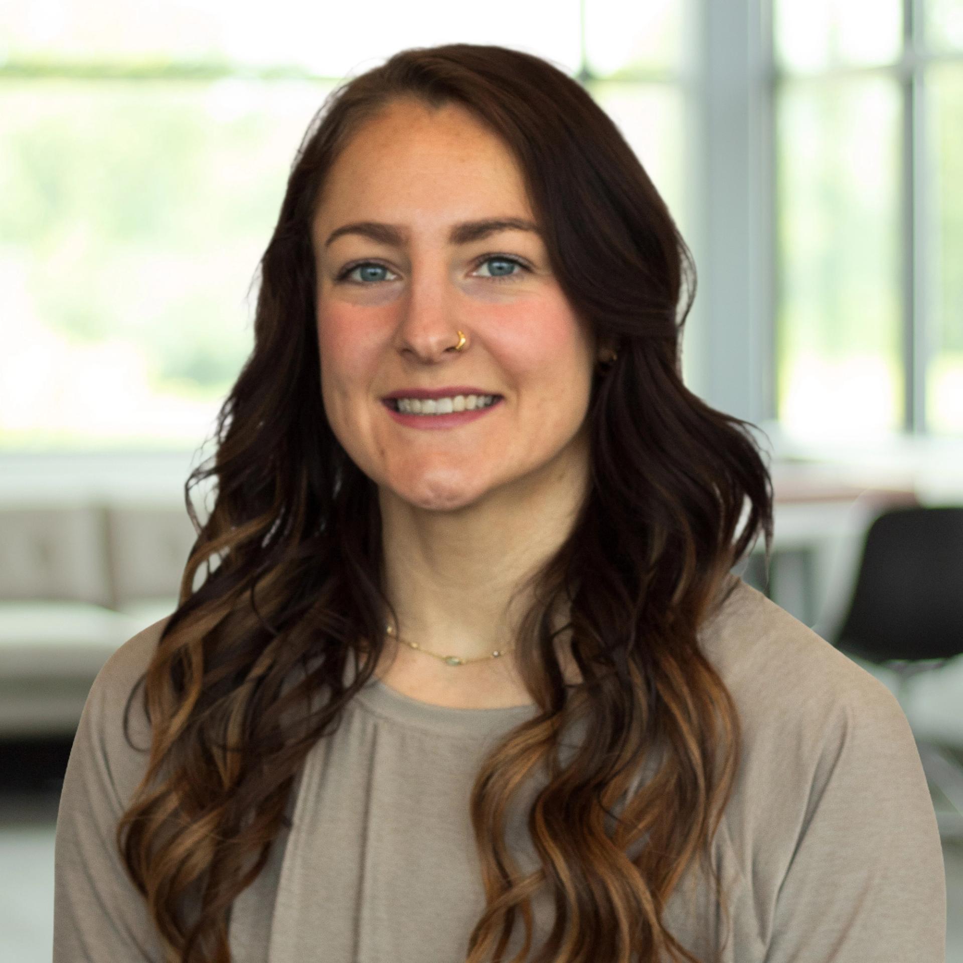 Hali Maye wearing a neutral top, smiling in a bright, modern office.