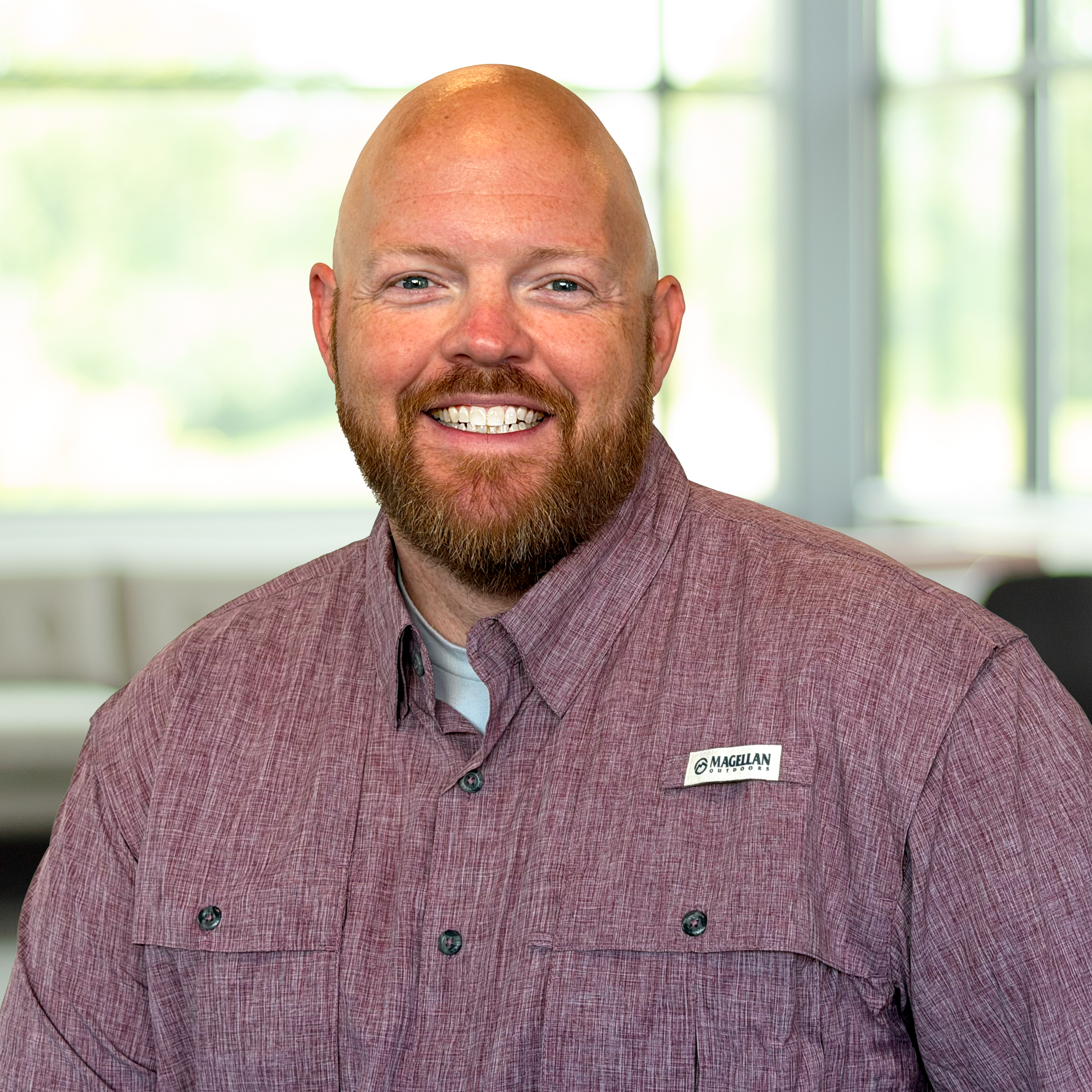 Bradley Opell, wearing a maroon button-up shirt, smiling in a bright, modern office.