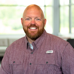 Bradley Opell, wearing a maroon button-up shirt, smiling in a bright, modern office.