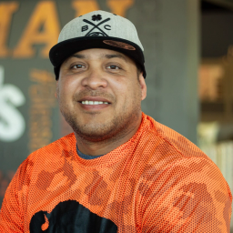 Haxer Gamez smiling in buffalo gear, standing in front of a company-branded wall.