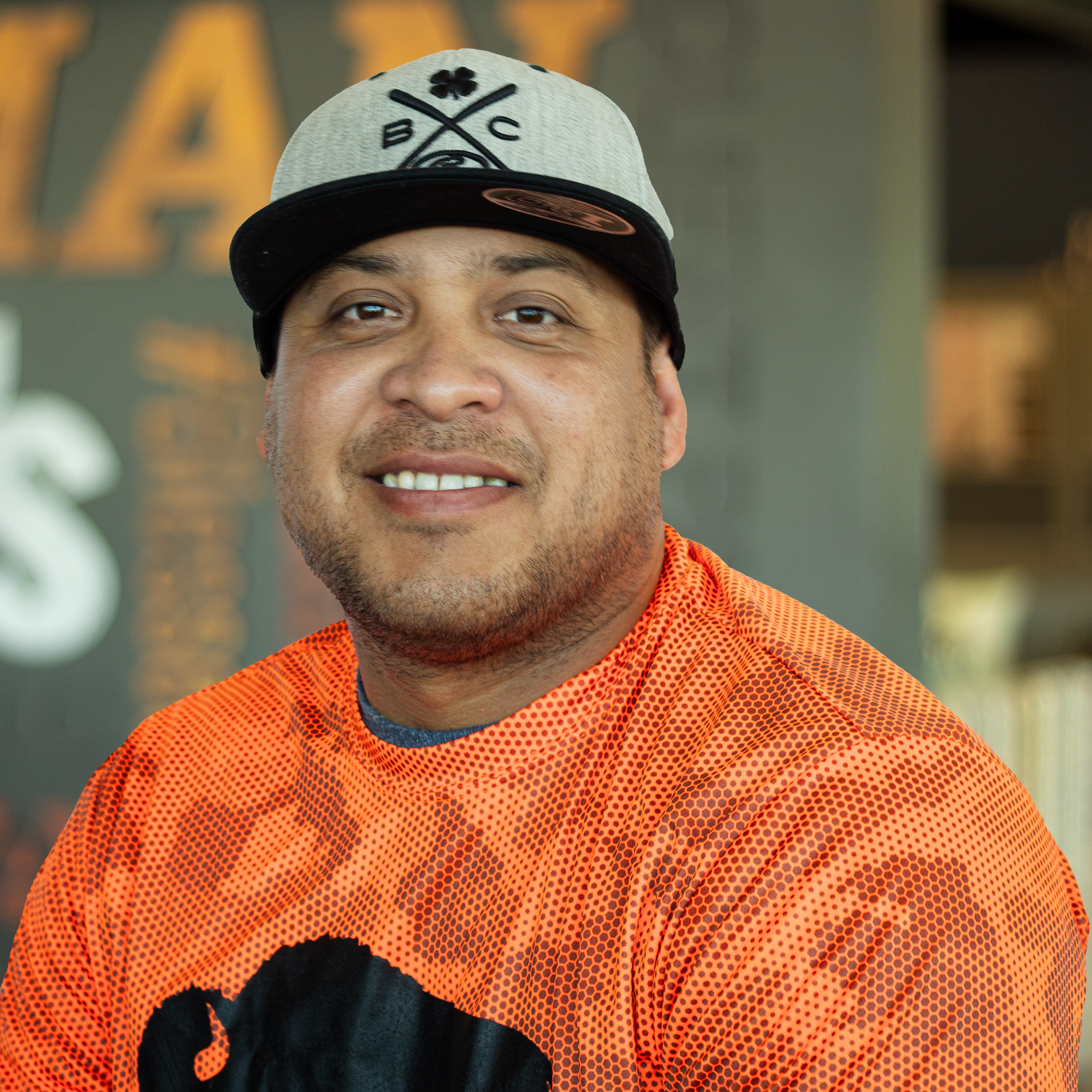 Haxer Gamez smiling in buffalo gear, standing in front of a company-branded wall.