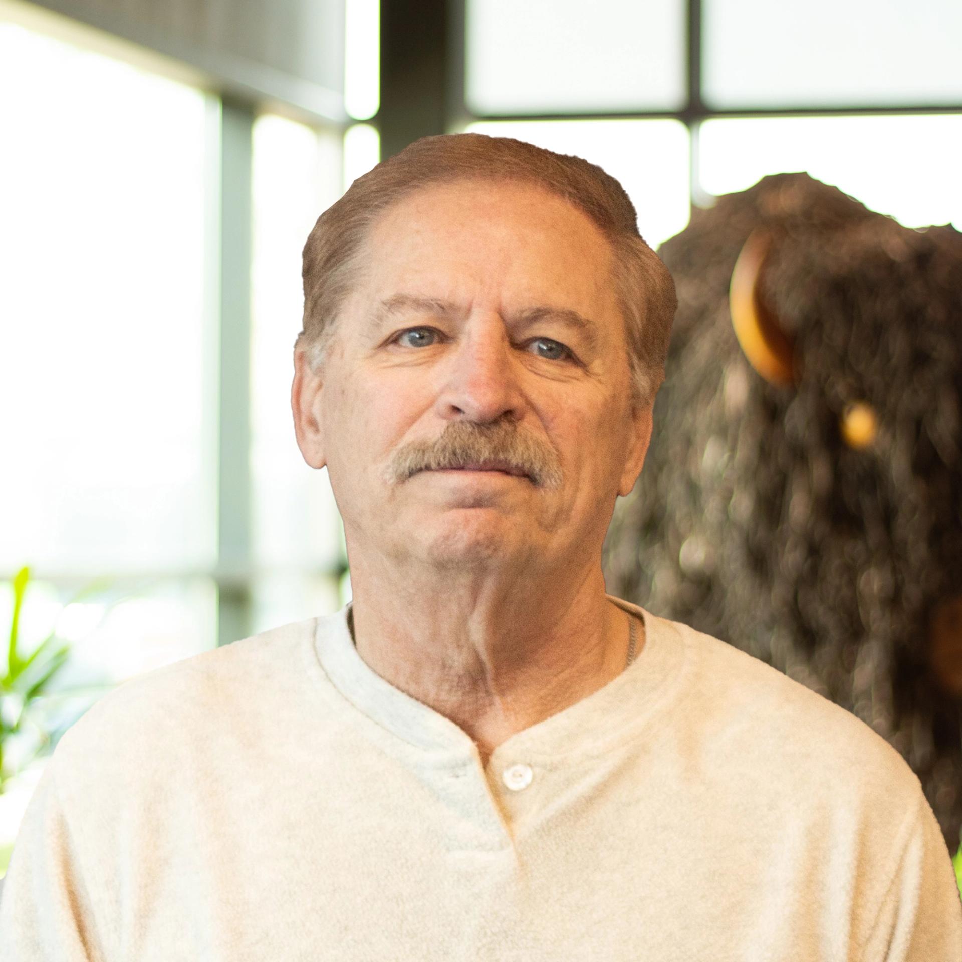 Kevin Stoughton smiling softly as they stand in front of a statue of a buffalo.