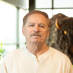 Kevin Stoughton smiling softly as they stand in front of a statue of a buffalo.