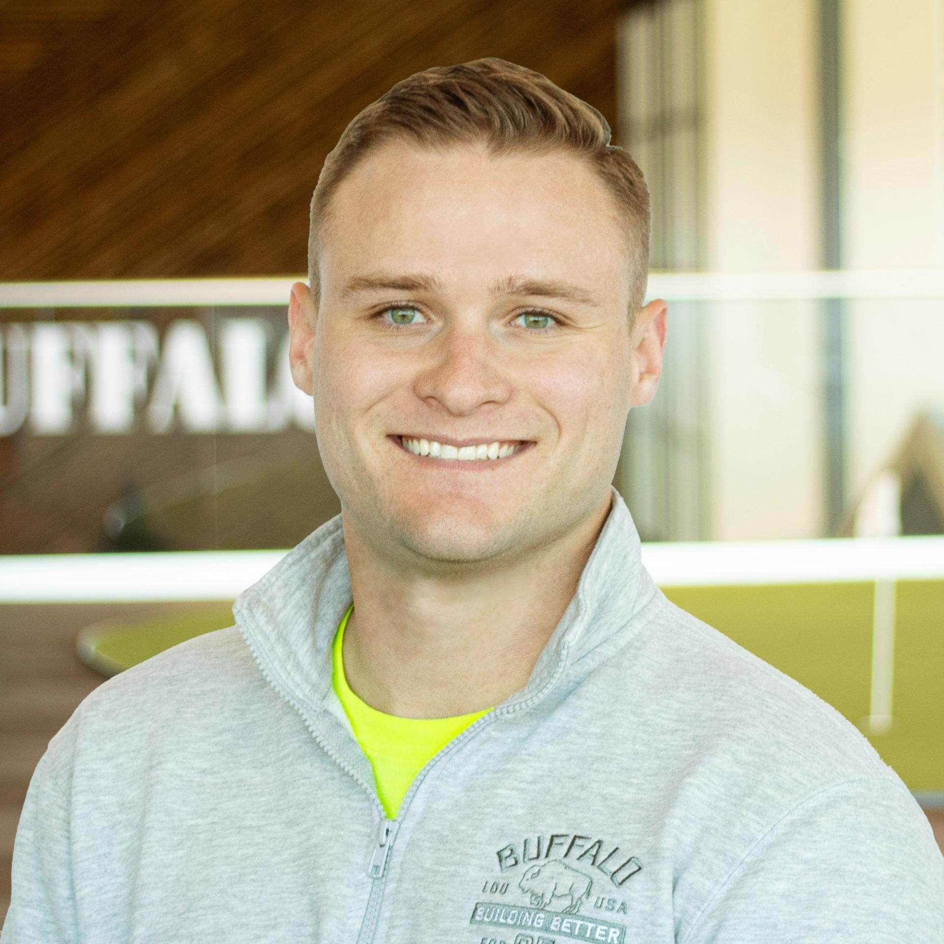 Mitchell Tulk smiling, wearing a buffalo branded pullover and standing in buffalo's office space.