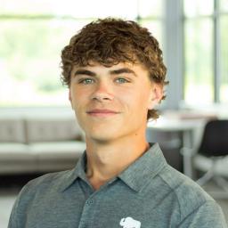 Carter Sturgeon smiles while wearing a gray Buffalo Construction polo in a bright, modern office with large windows.