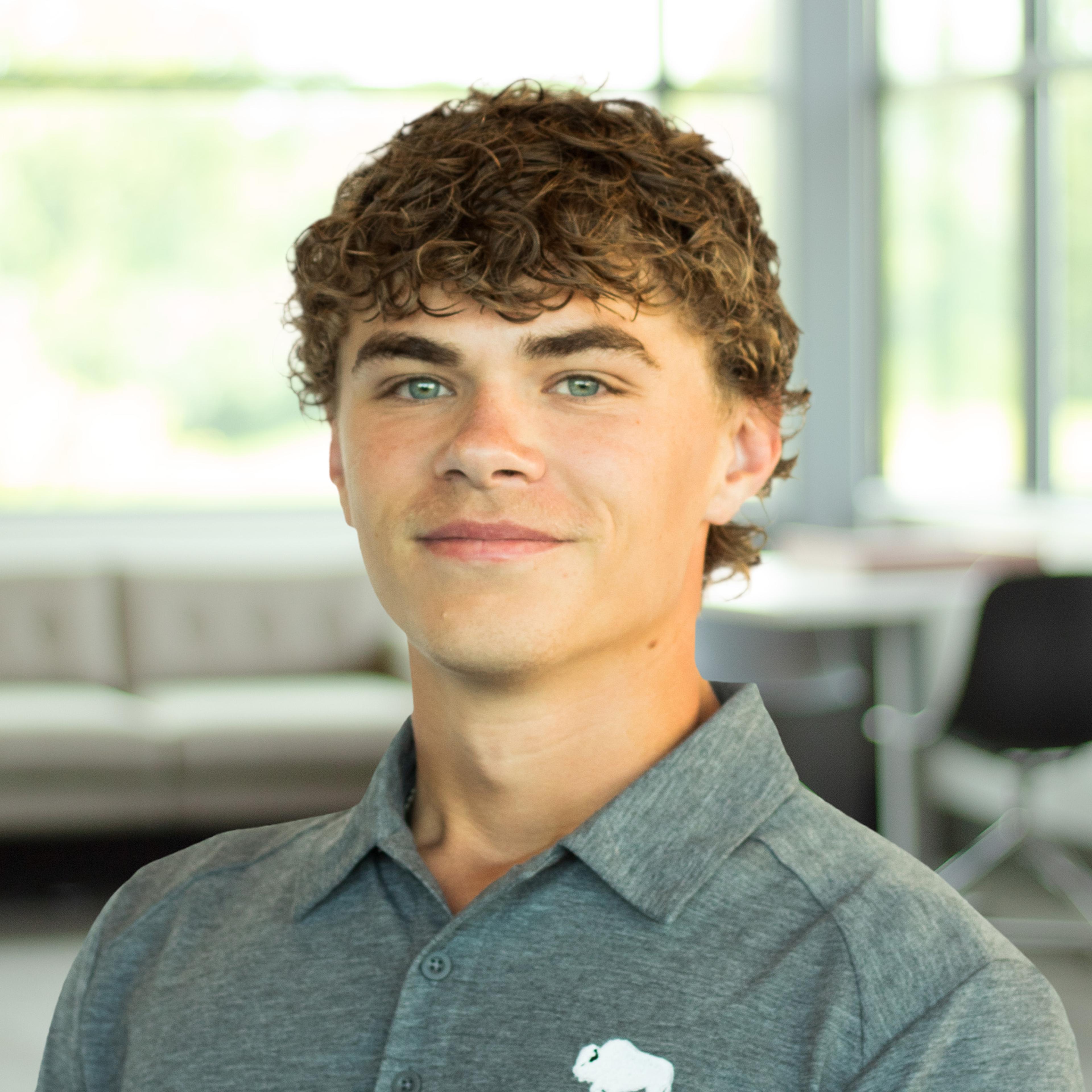 Carter Sturgeon smiles while wearing a gray Buffalo Construction polo in a bright, modern office with large windows.