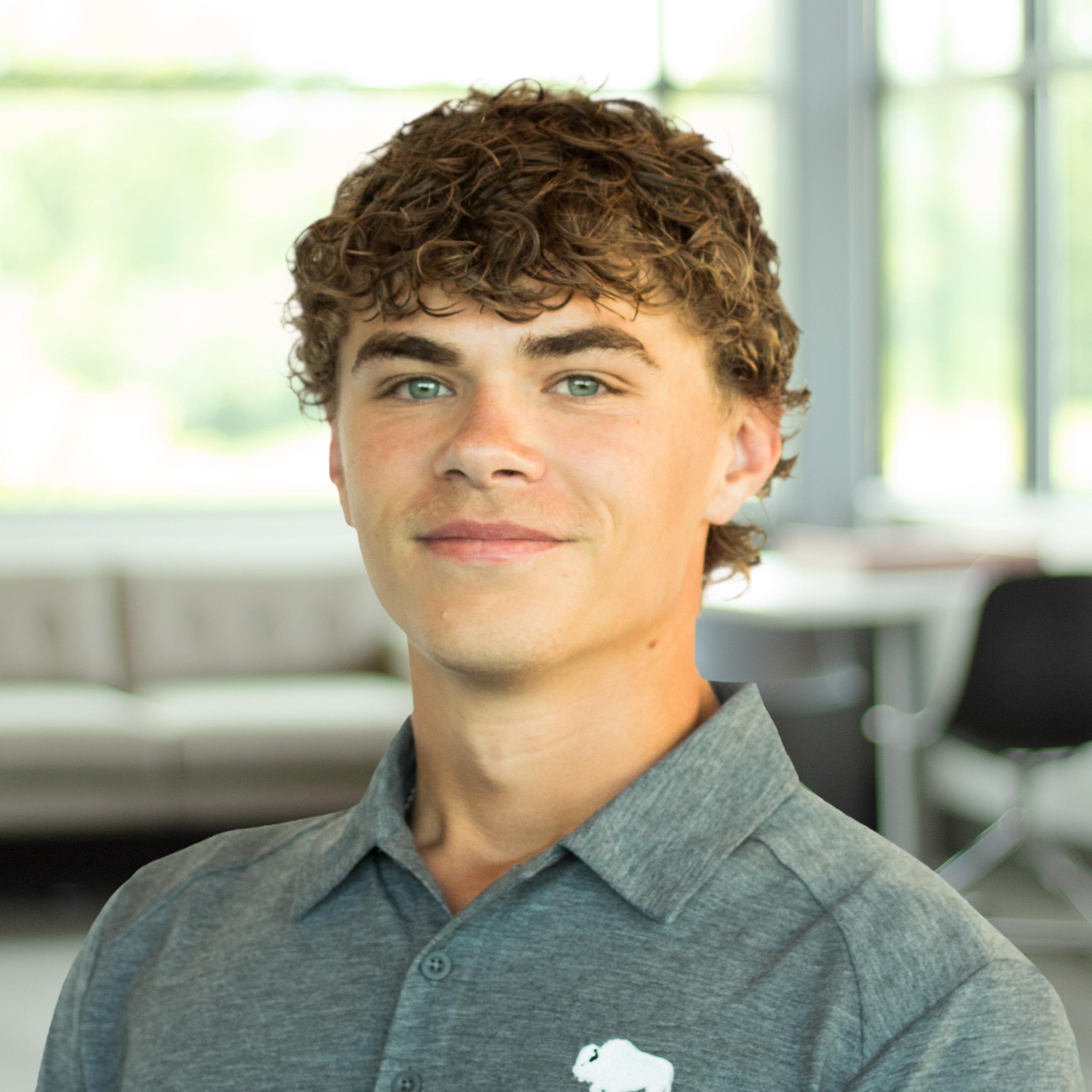Carter Sturgeon smiles while wearing a gray Buffalo Construction polo in a bright, modern office with large windows.