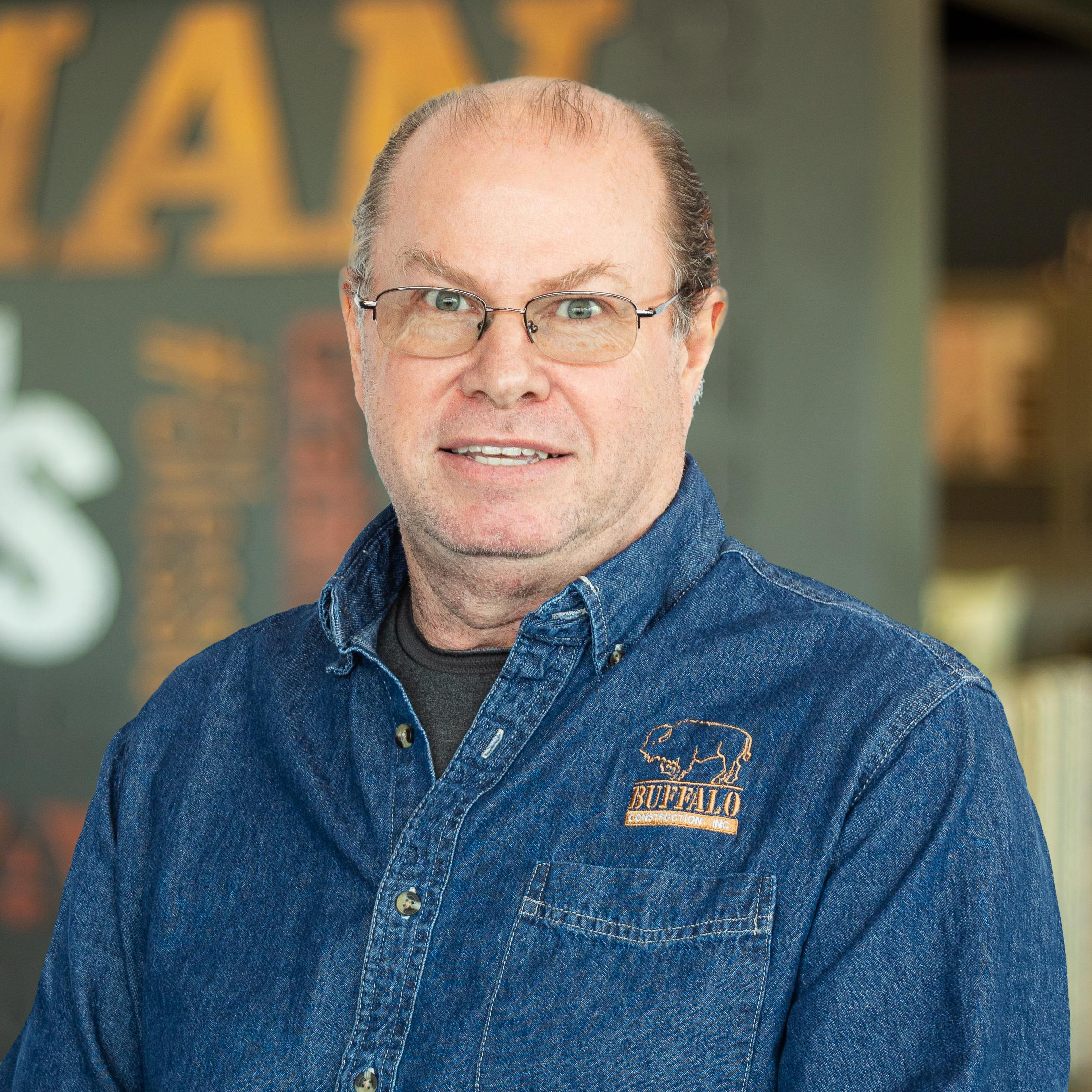 Philip "Krusty" Gamez wearing a buffalo branded button down and standing in front of a company-branded wall.