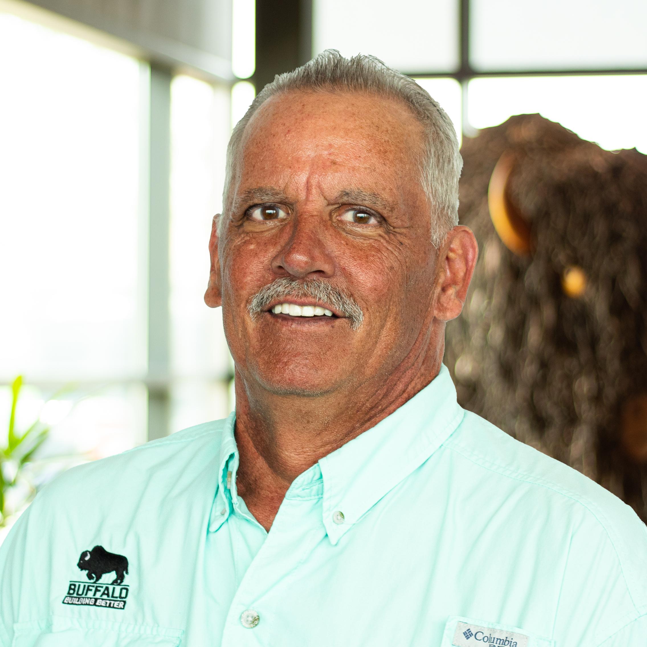 Paul Hess giving a smile in a bright mint green buffalo branded shirt, standing in front of the Roman A. Buffalo sculpture.