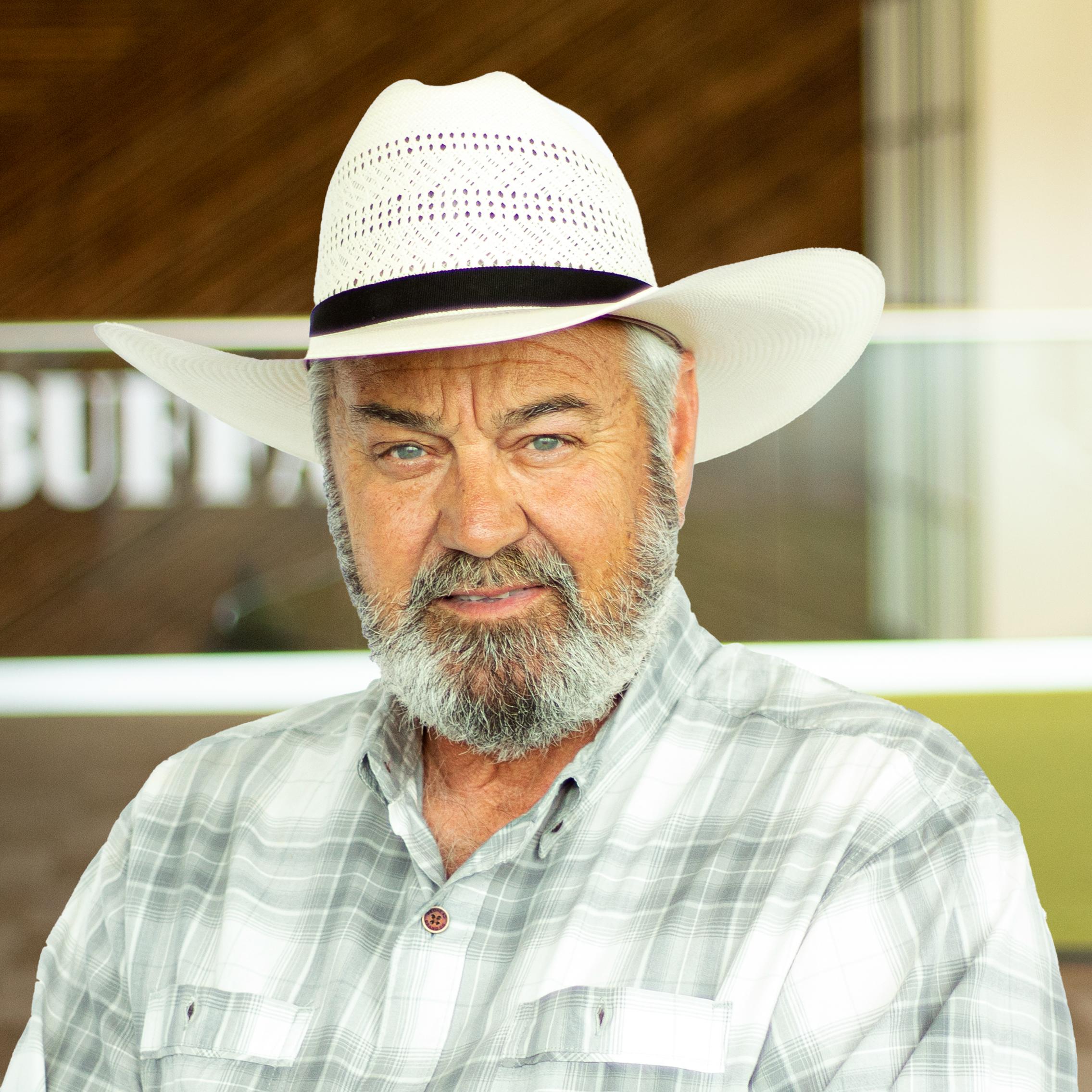 Bill Mattli wearing a white cowboy hat with a smirk, standing in buffalo's office space.
