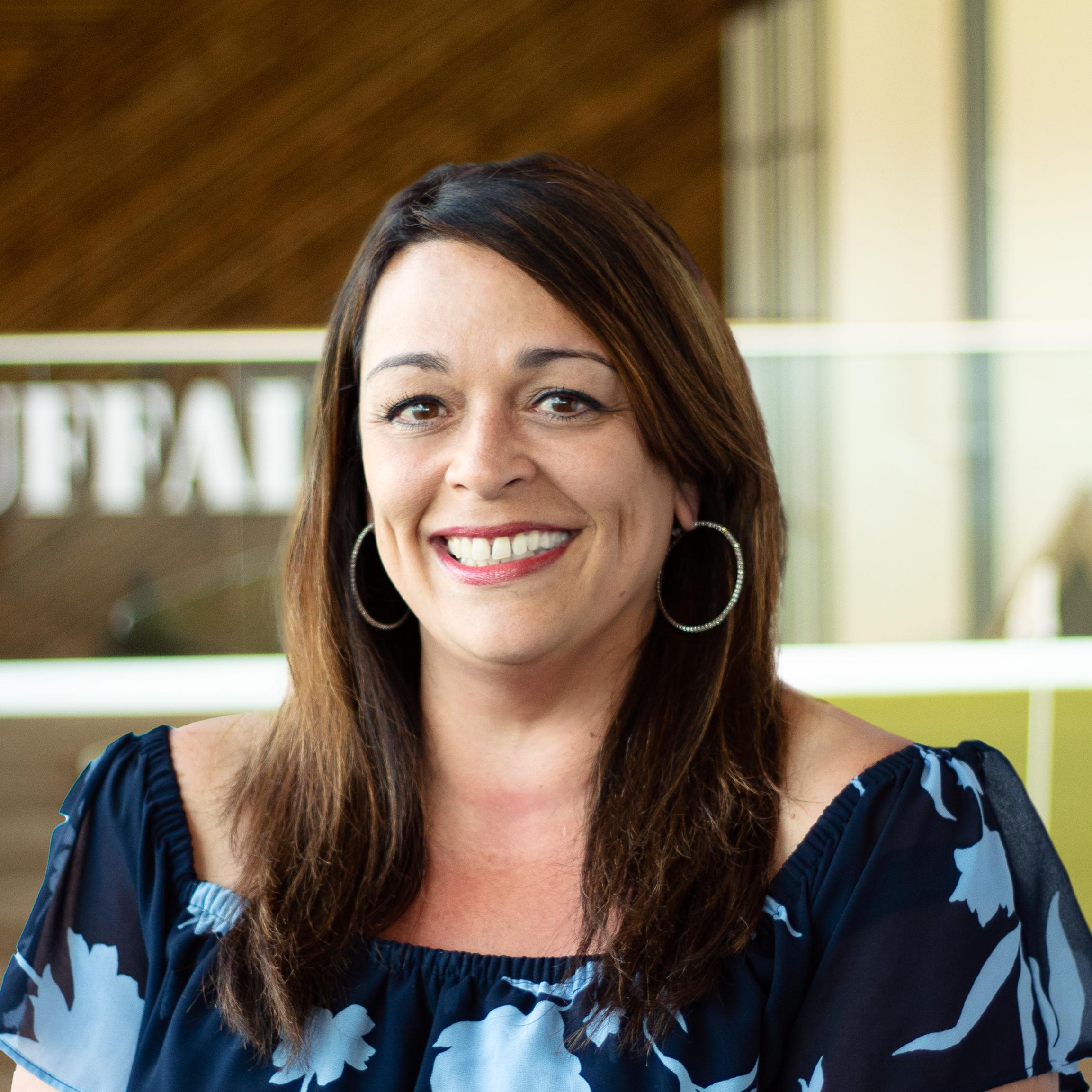 Jennifer Pineda smiling, wearing a floral top, standing in buffalo's office space.
