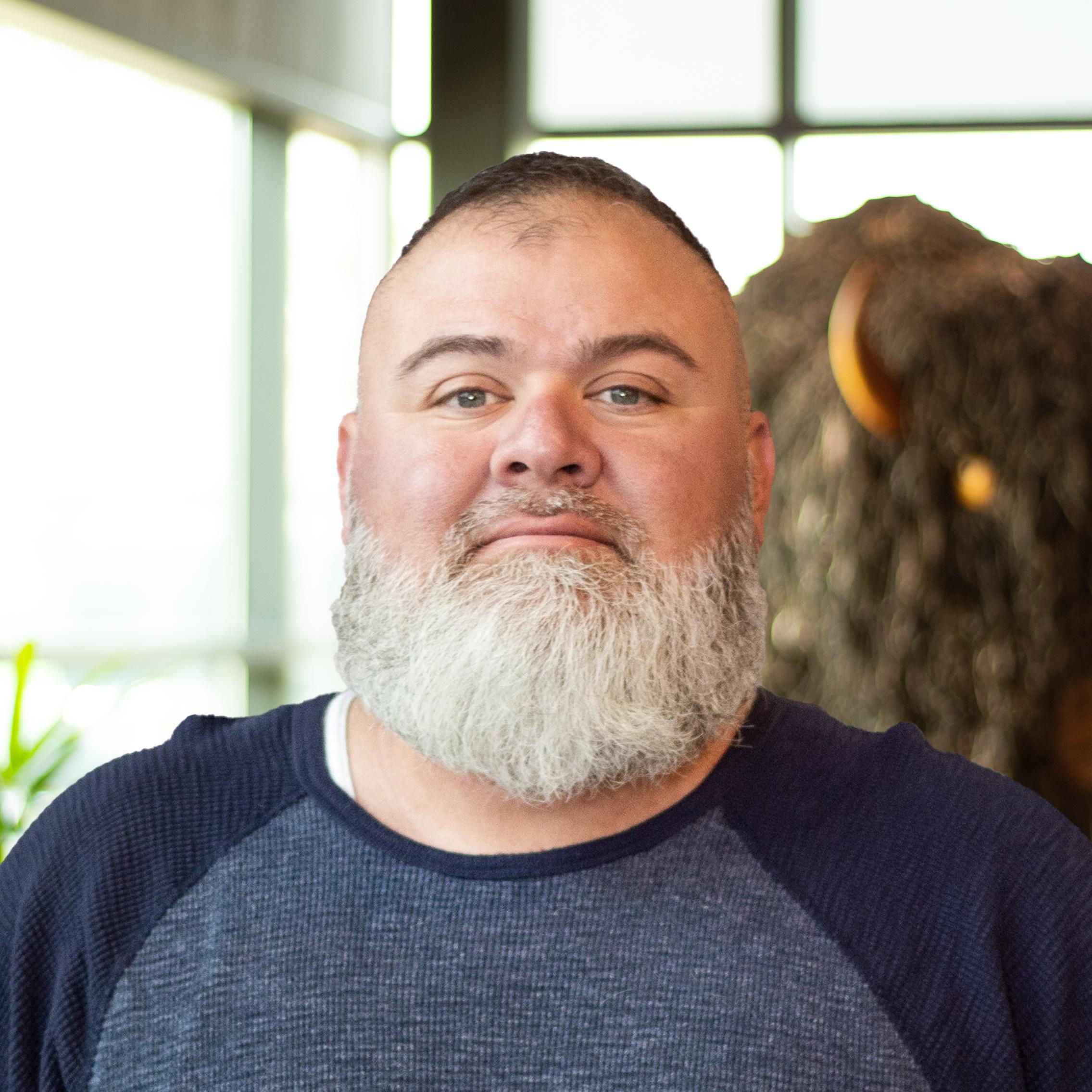 Ed Cazares with a slight smile as they stand in front of a statue of a buffalo.