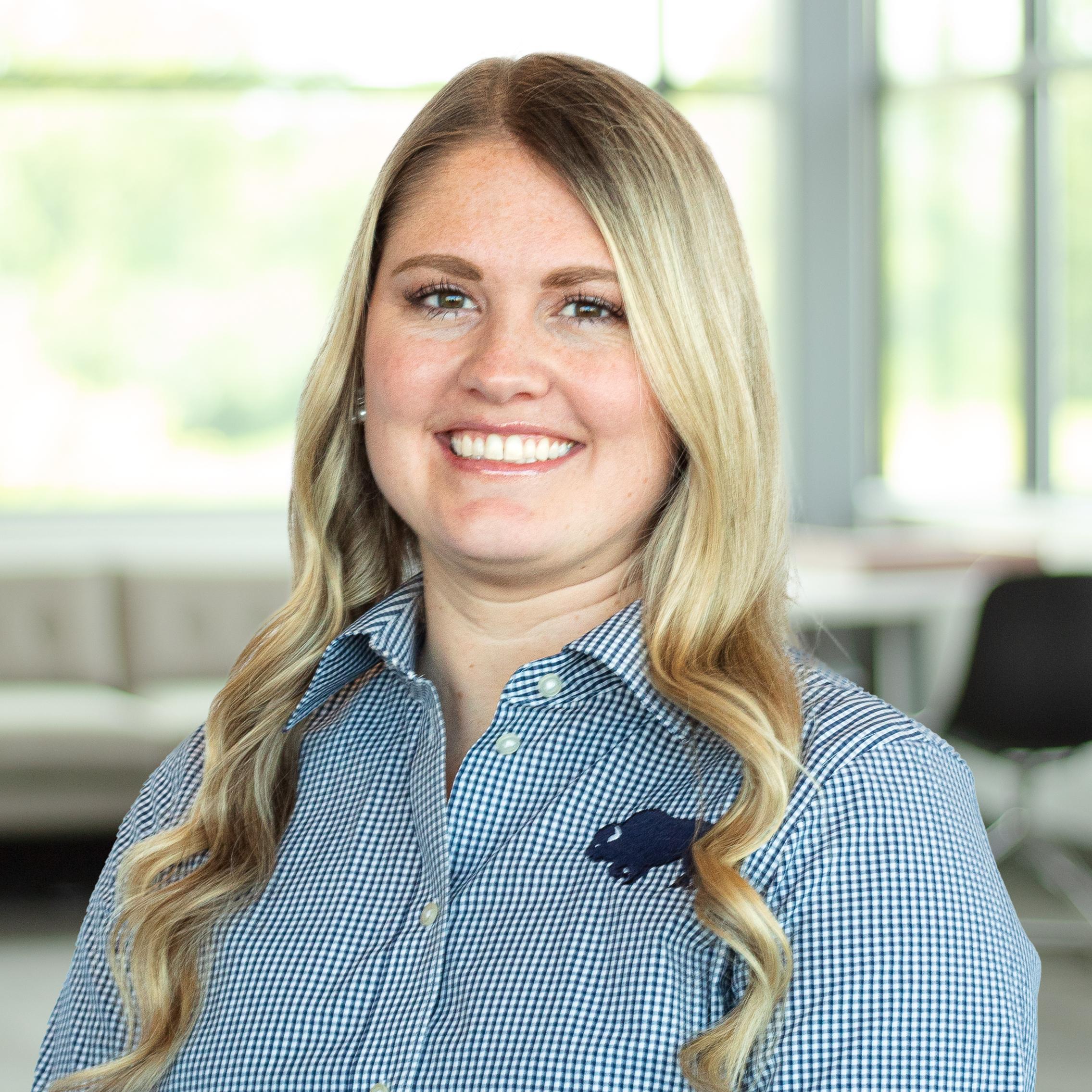 Jessica Wafzig wearing a plaid buffalo branded button down, smiling in a bright, modern office.