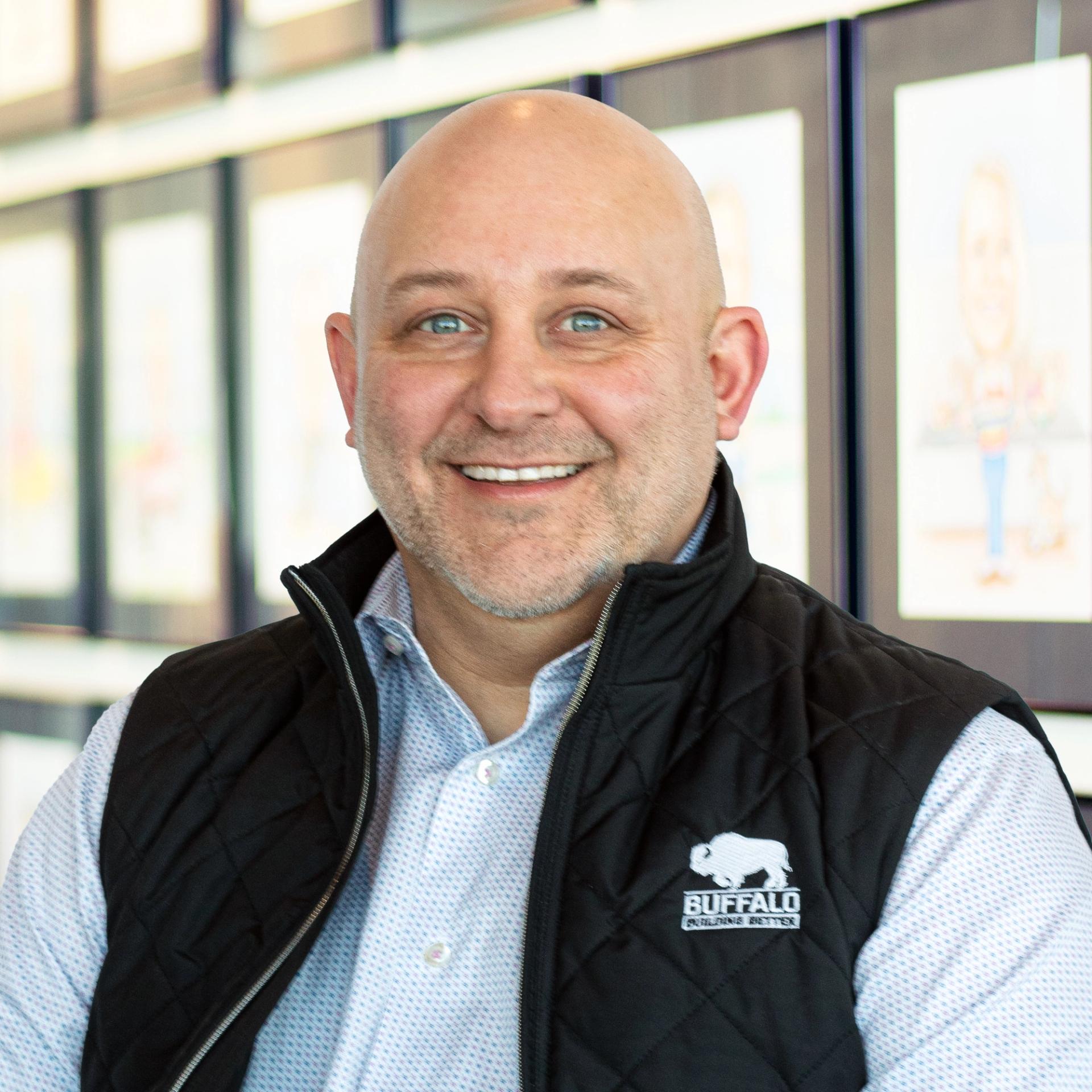 Jason Aberli wearing a smile, standing in front of a wall displaying framed caricatures.