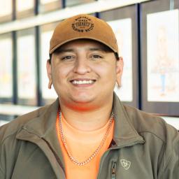 David Rodriguez wearing a bright orange shirt and standing in front of a wall displaying framed caricatures.