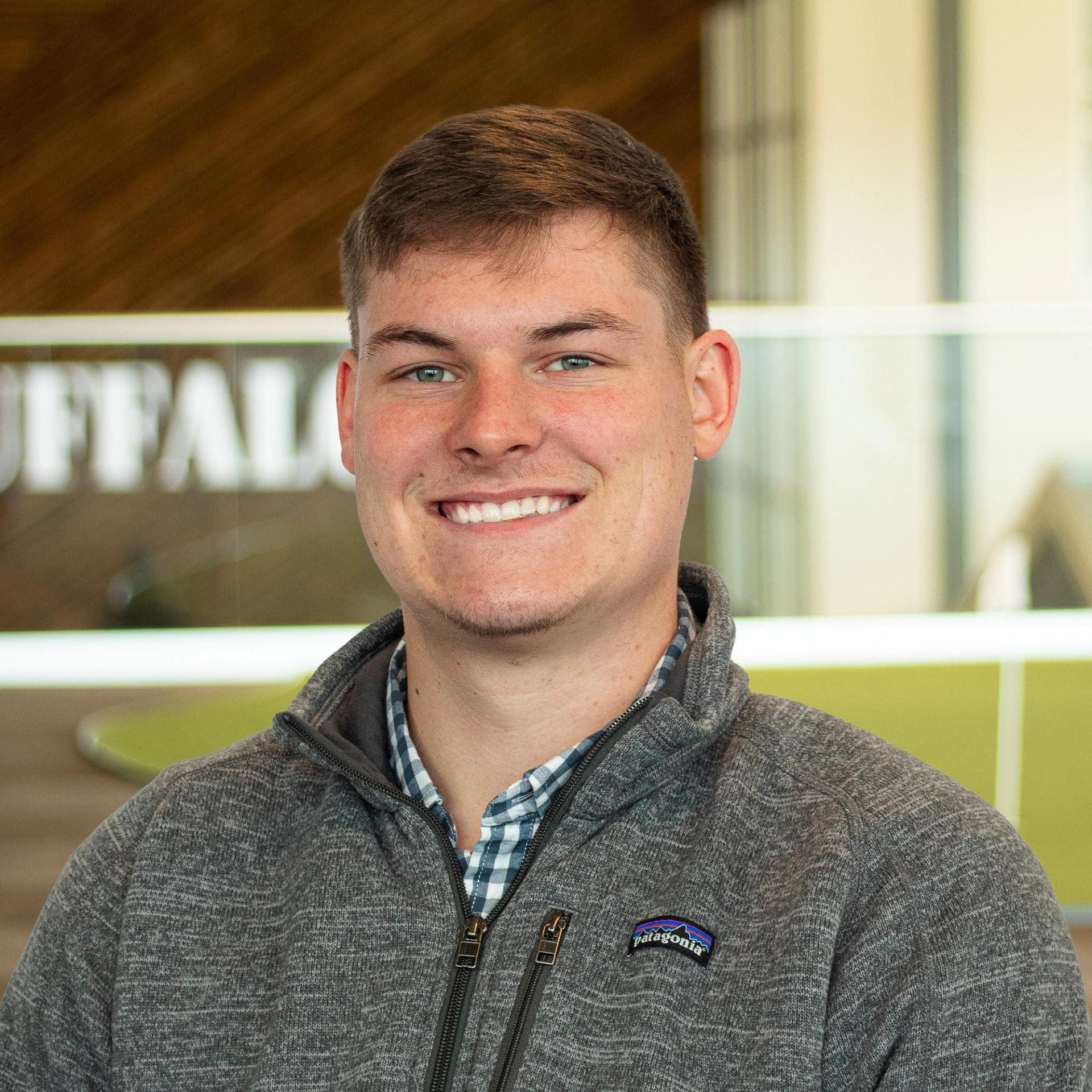 Matthew Frazier smiling, wearing a gray jacket, standing in buffalo's office space.