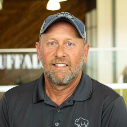 Brian Blank giving a hint of a smile, while wearing a gray buffalo branded polo standing in buffalo's office space.