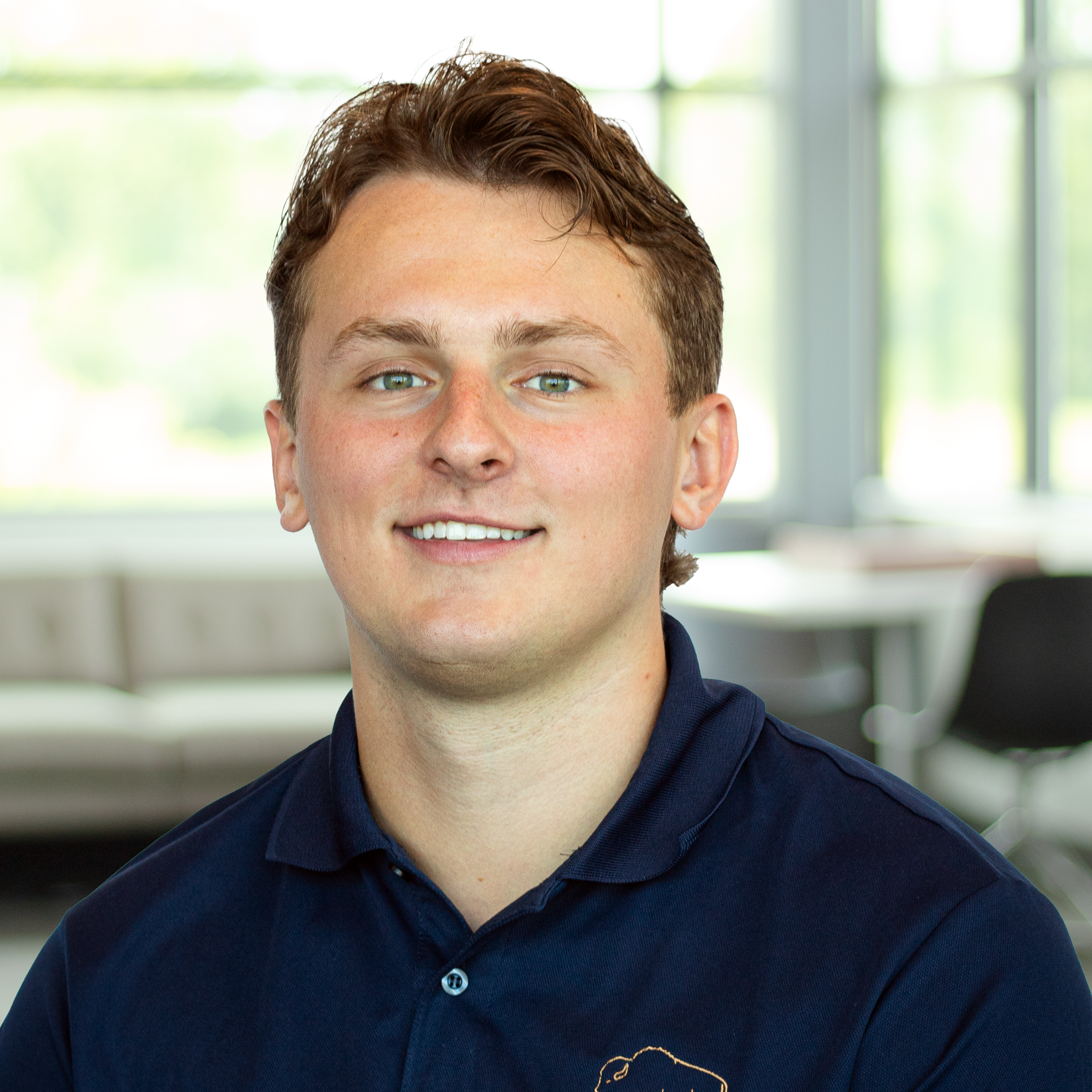 Nick Duffey wearing a buffalo branded polo and smiling softly in a bright, modern office.