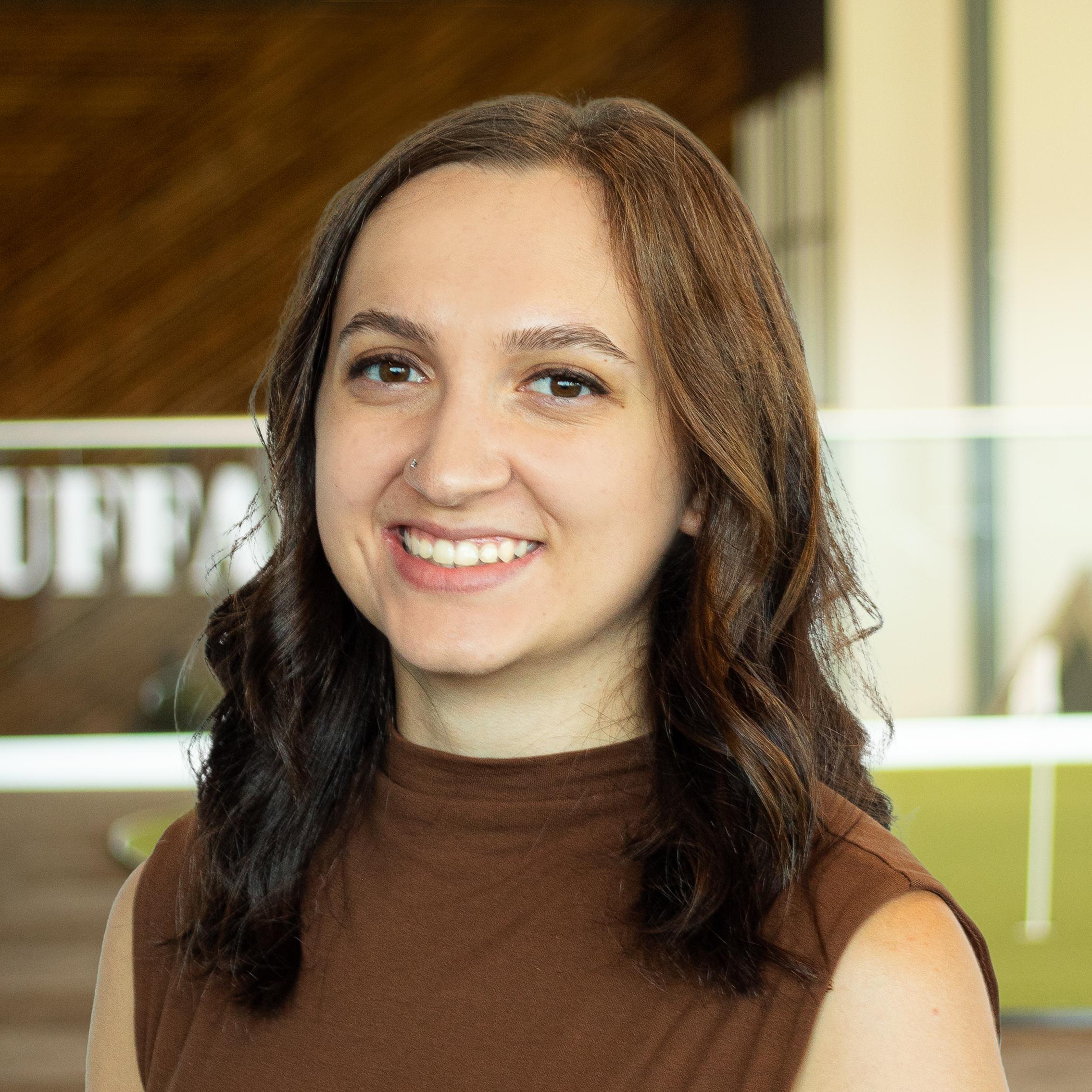 Kayla Puffer, wearing a sleeveless brown top, smiling in a bright, modern office.