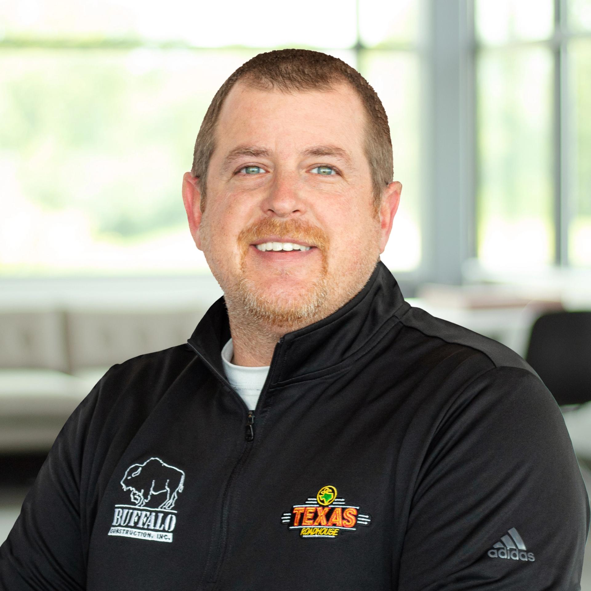 Brad Rigney wearing a Texas Roadhouse and buffalo branded sweater and smiling in a bright, modern office.
