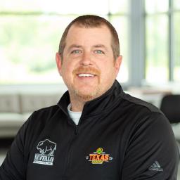 Brad Rigney wearing a Texas Roadhouse and buffalo branded sweater and smiling in a bright, modern office.