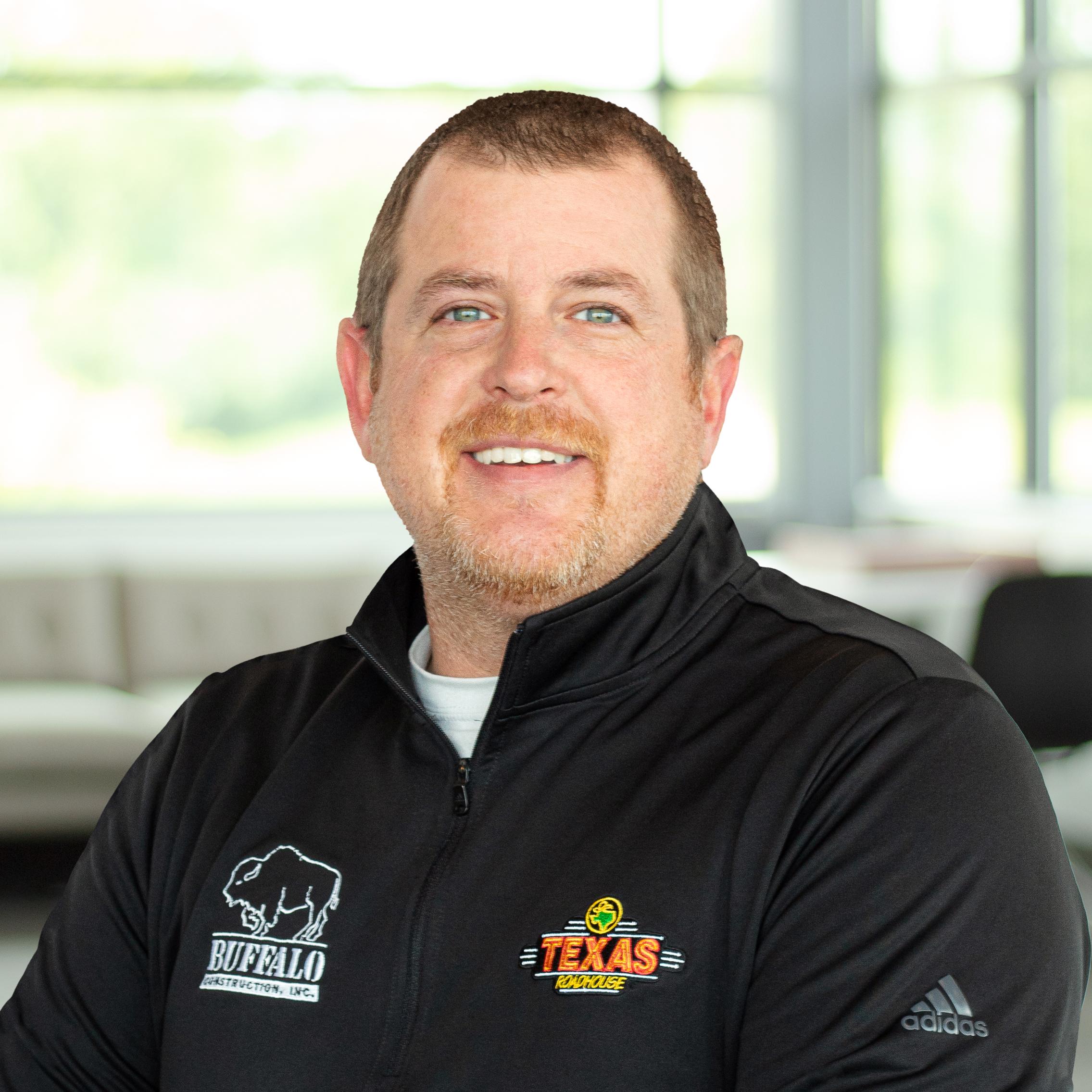 Brad Rigney wearing a Texas Roadhouse and buffalo branded sweater and smiling in a bright, modern office.