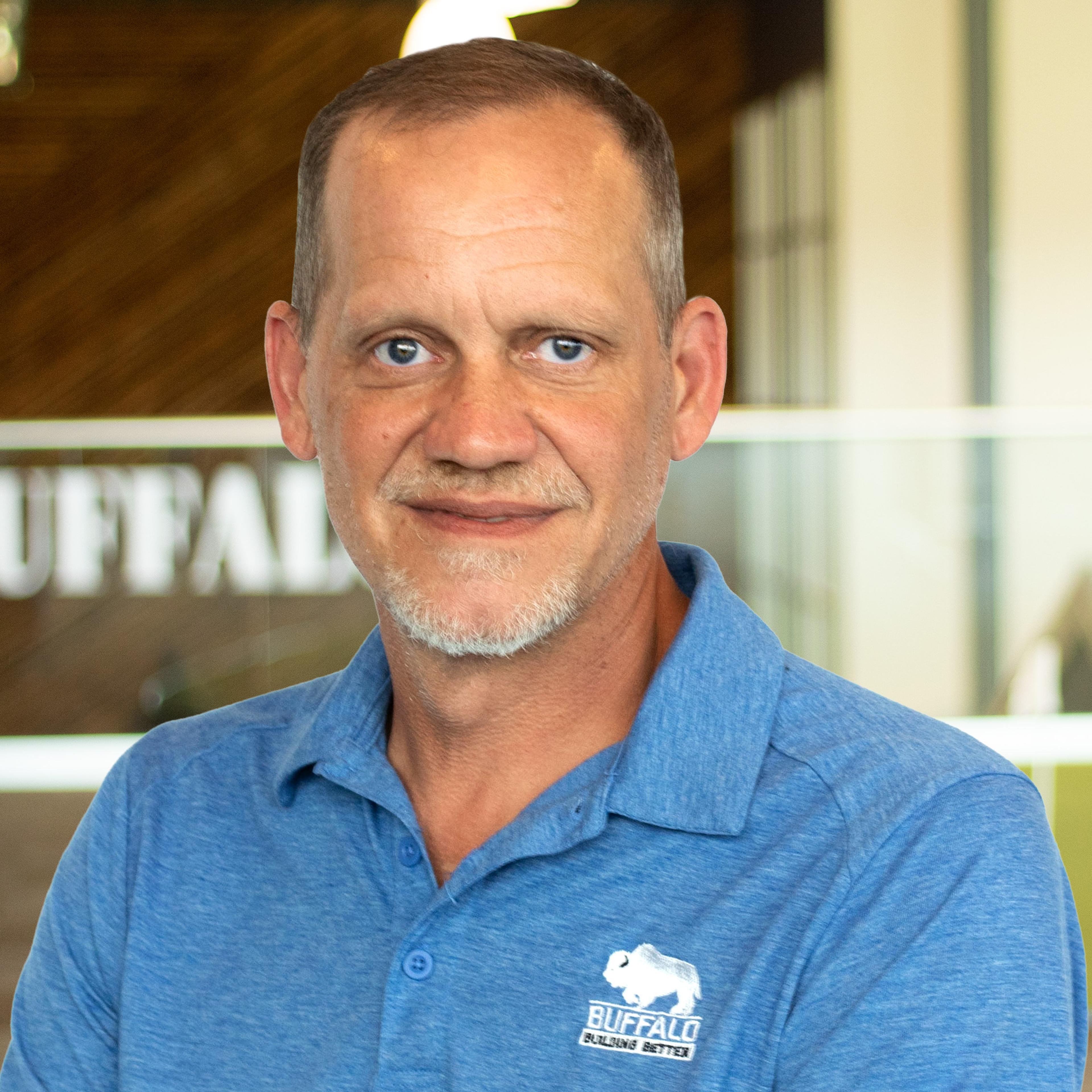 Billy Stiles smiling, wearing a blue Buffalo Construction polo, standing in Buffalo's office space.