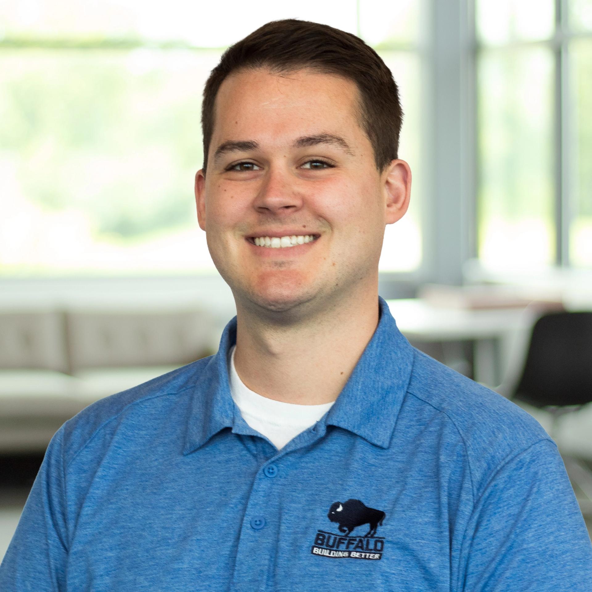 Nick Thomas wearing a blue Buffalo polo, standing in a bright office space.