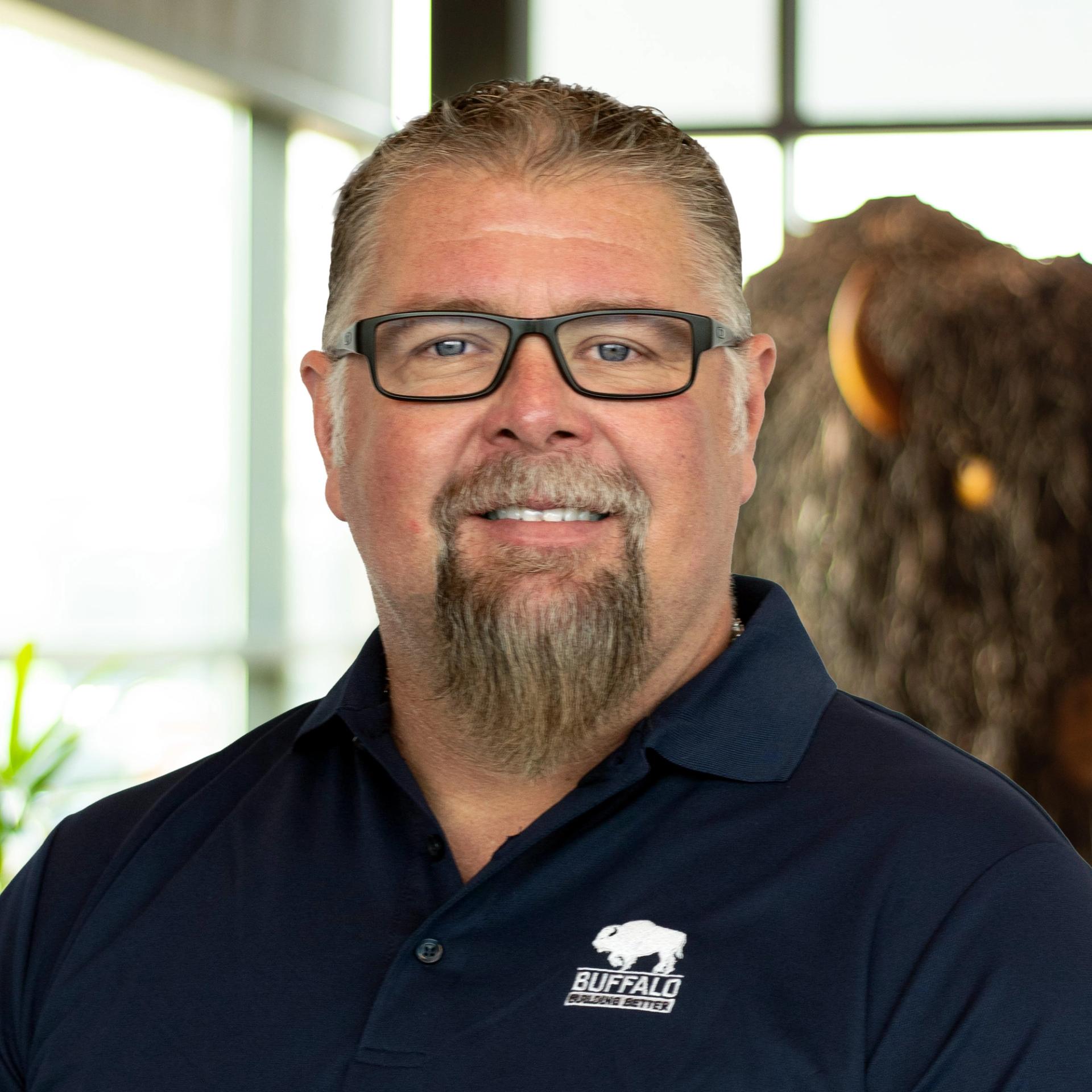 Bobby Clark smiling wearing a navy blue buffalo polo as he stands in front of a statue of a buffalo.