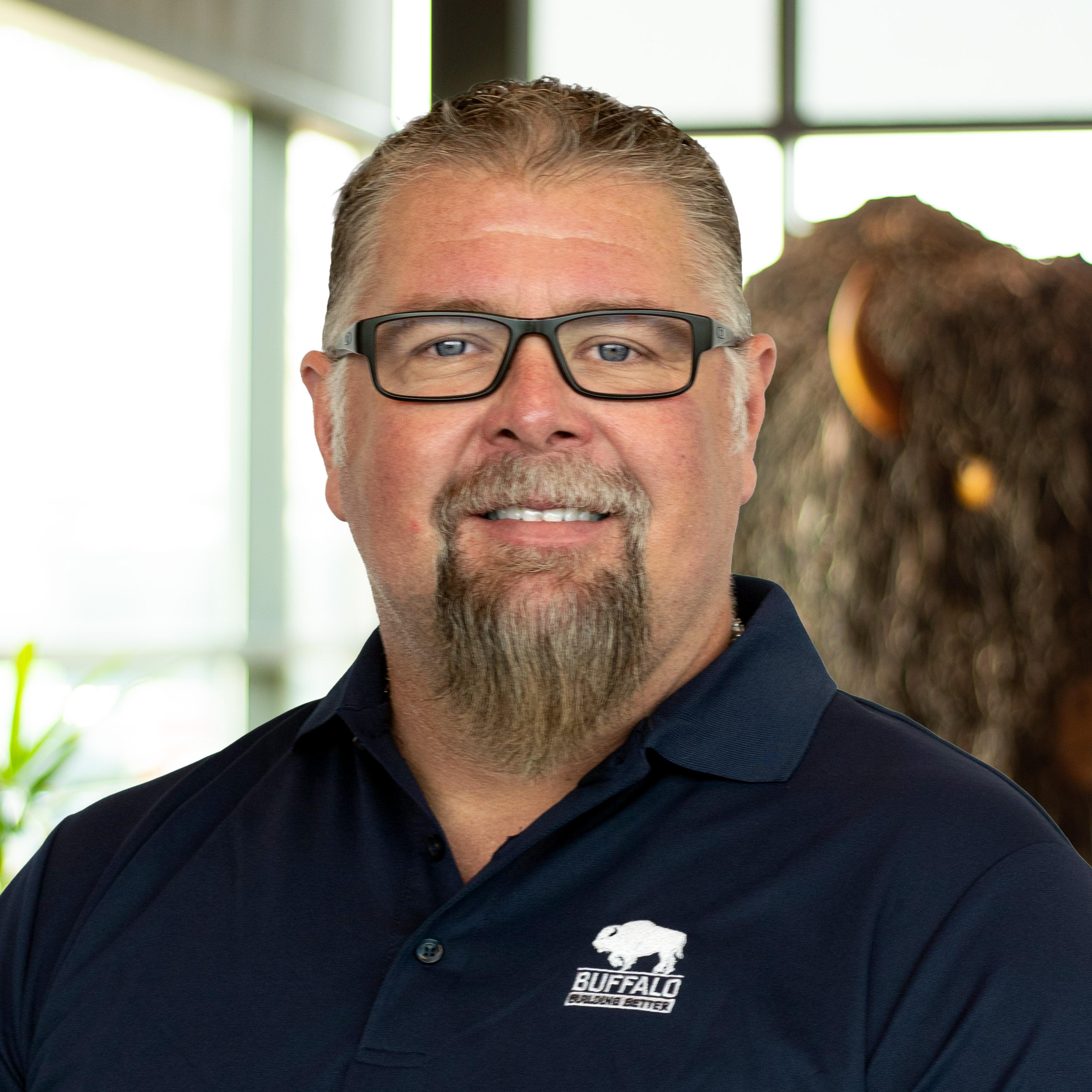 Bobby Clark smiling wearing a navy blue buffalo polo as he stands in front of a statue of a buffalo.