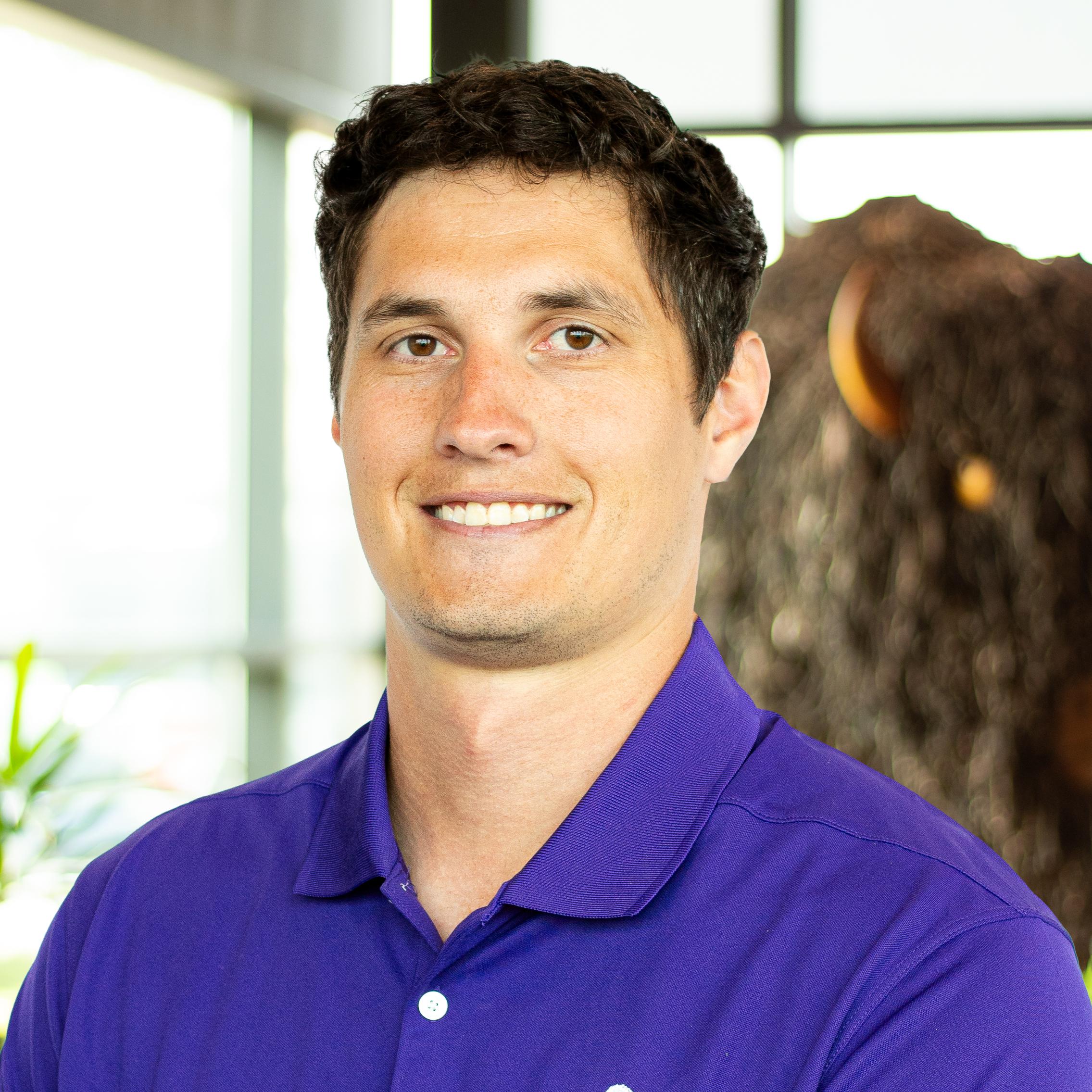 Ryan Mayorga smiling as they stand in front of a statue of a buffalo.