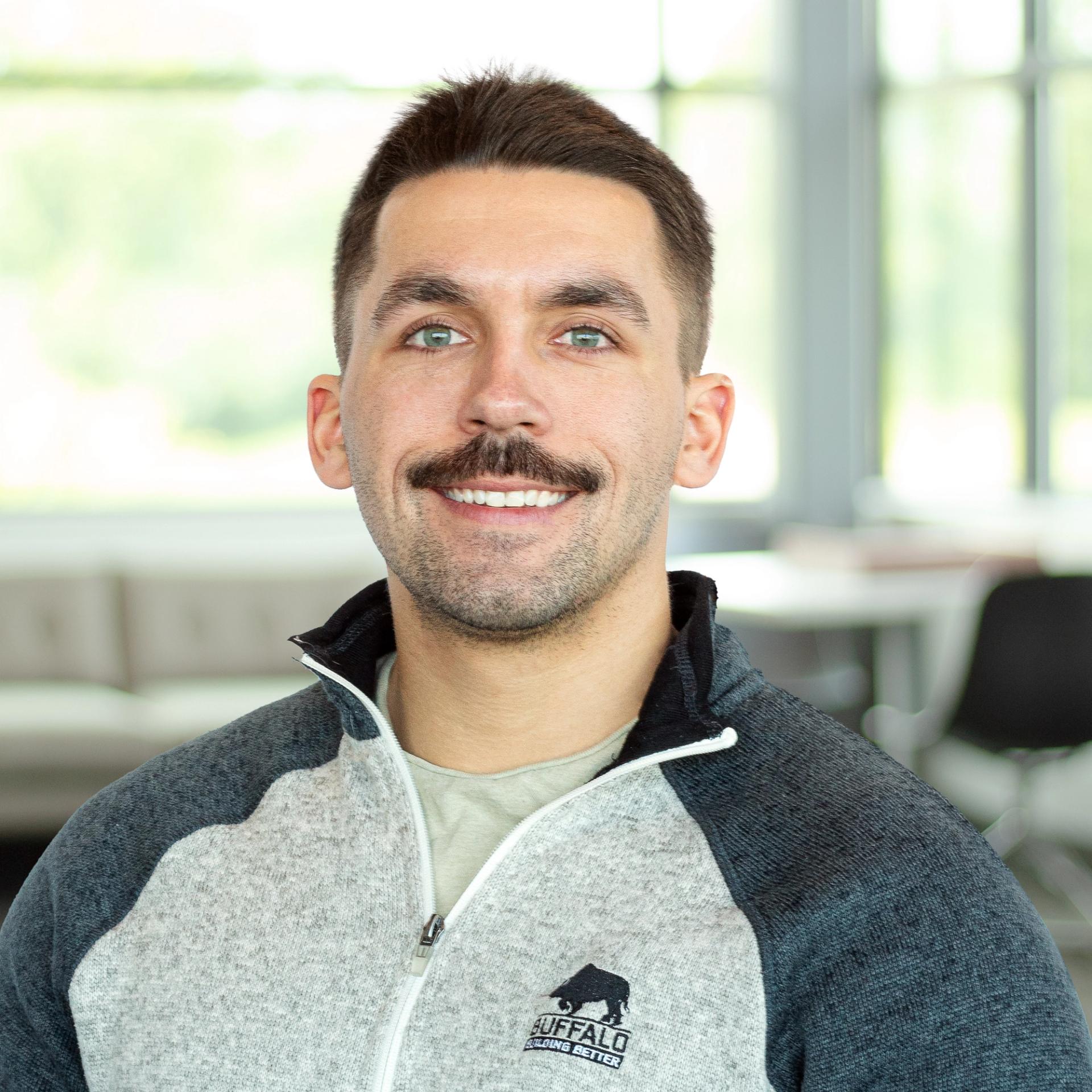 TJ Cole wearing a buffalo branded sweater, smiling in a bright, modern office.